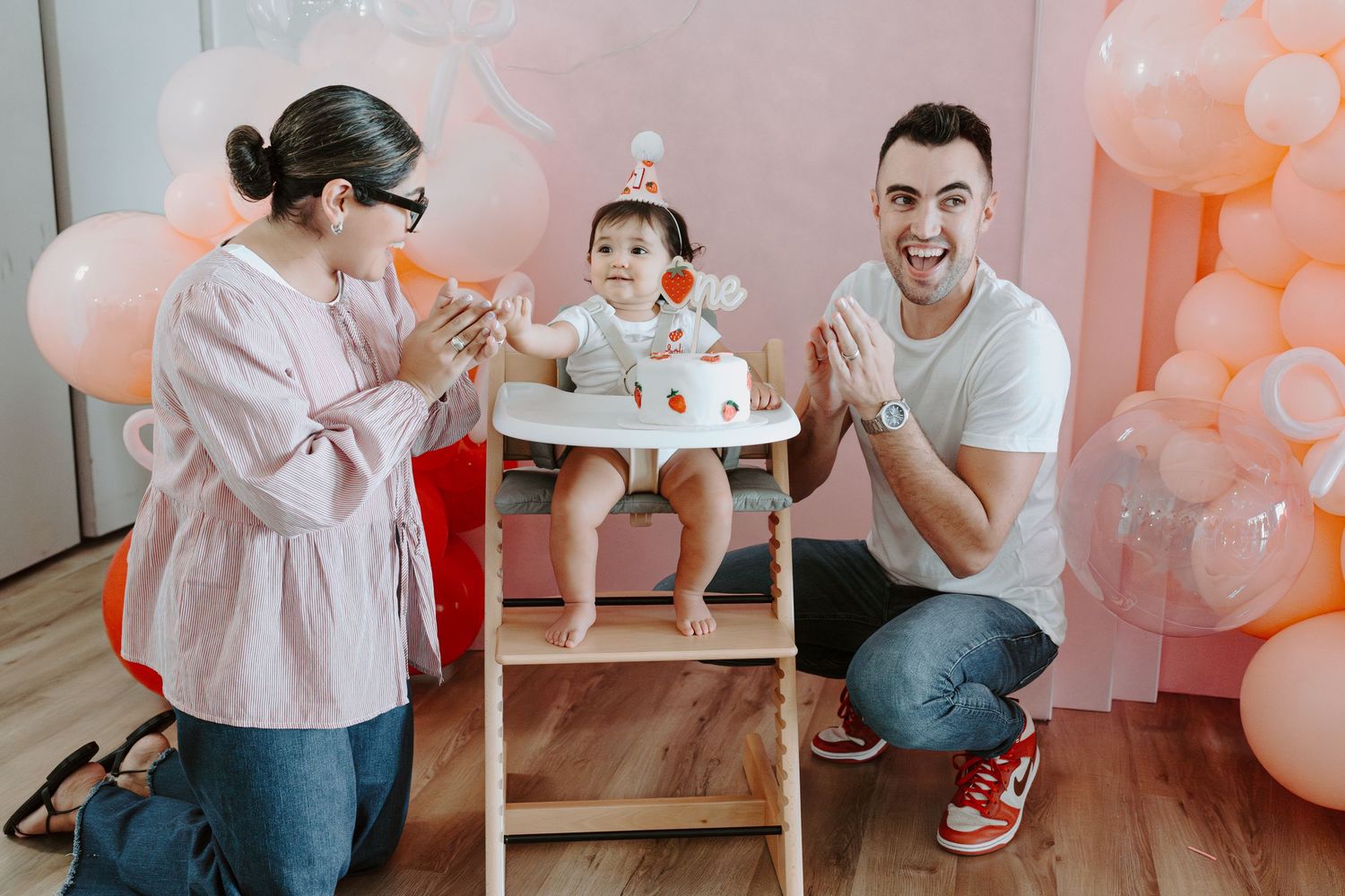 Birthday party scene with balloon arch and illuminated signage in pink tones.