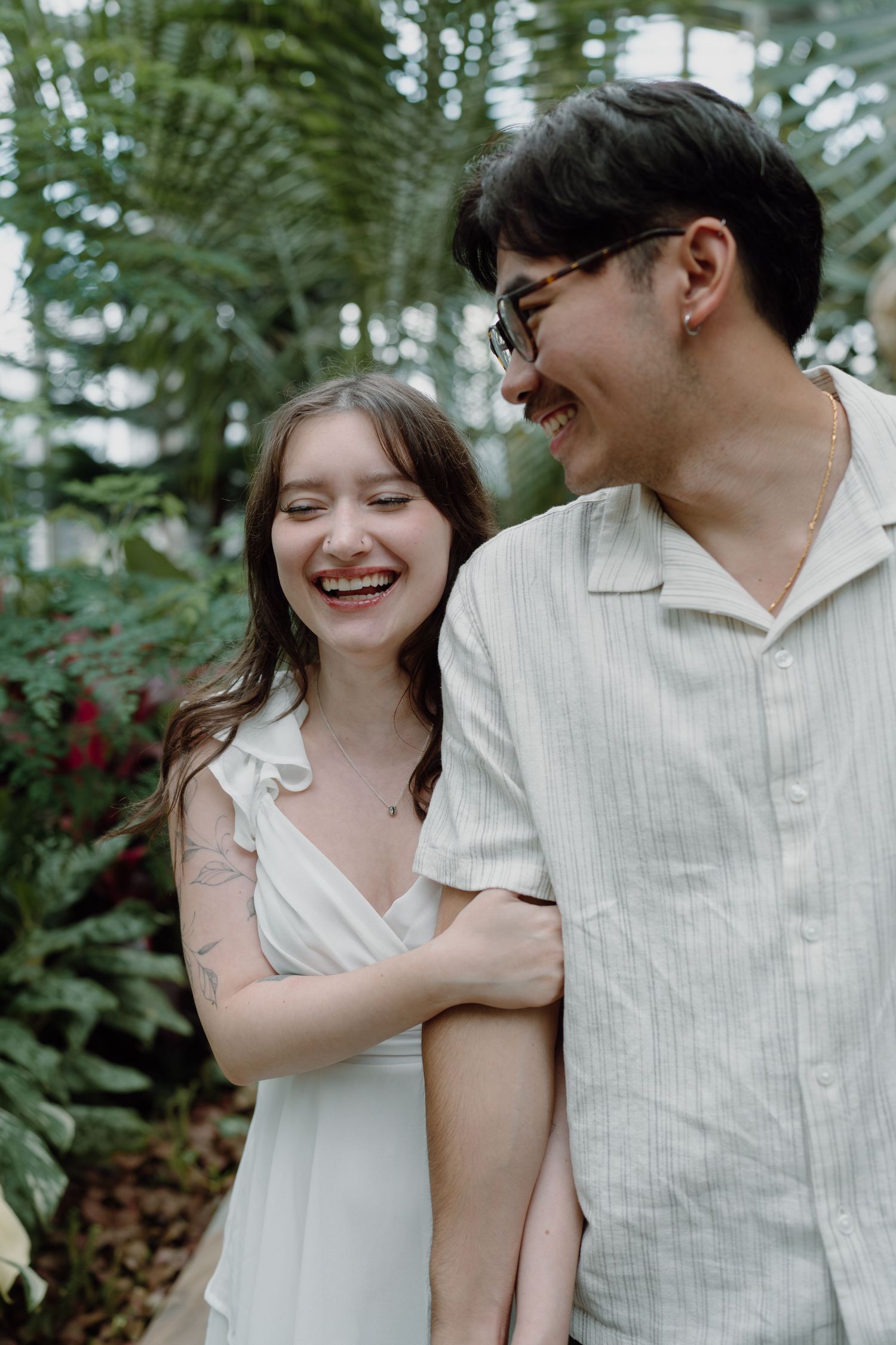 A romantic couple in white outfits share tender moments against a lush garden backdrop.