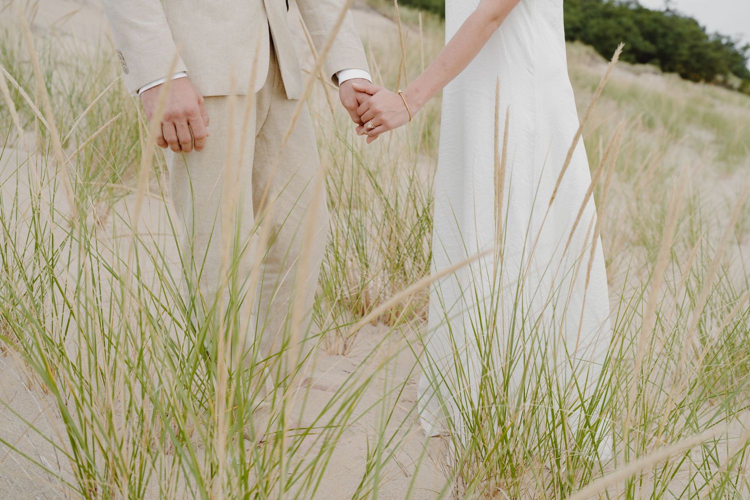 Romantic beach photoshoot with couple in light colored formal wear among dune grass.