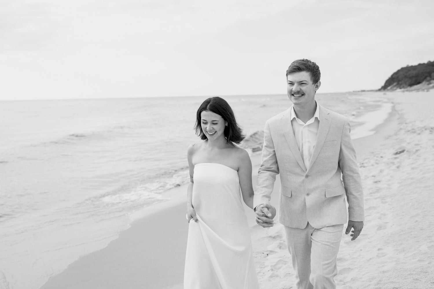 Joyful moment captured of a couple walking along a scenic beach with coastal vegetation.