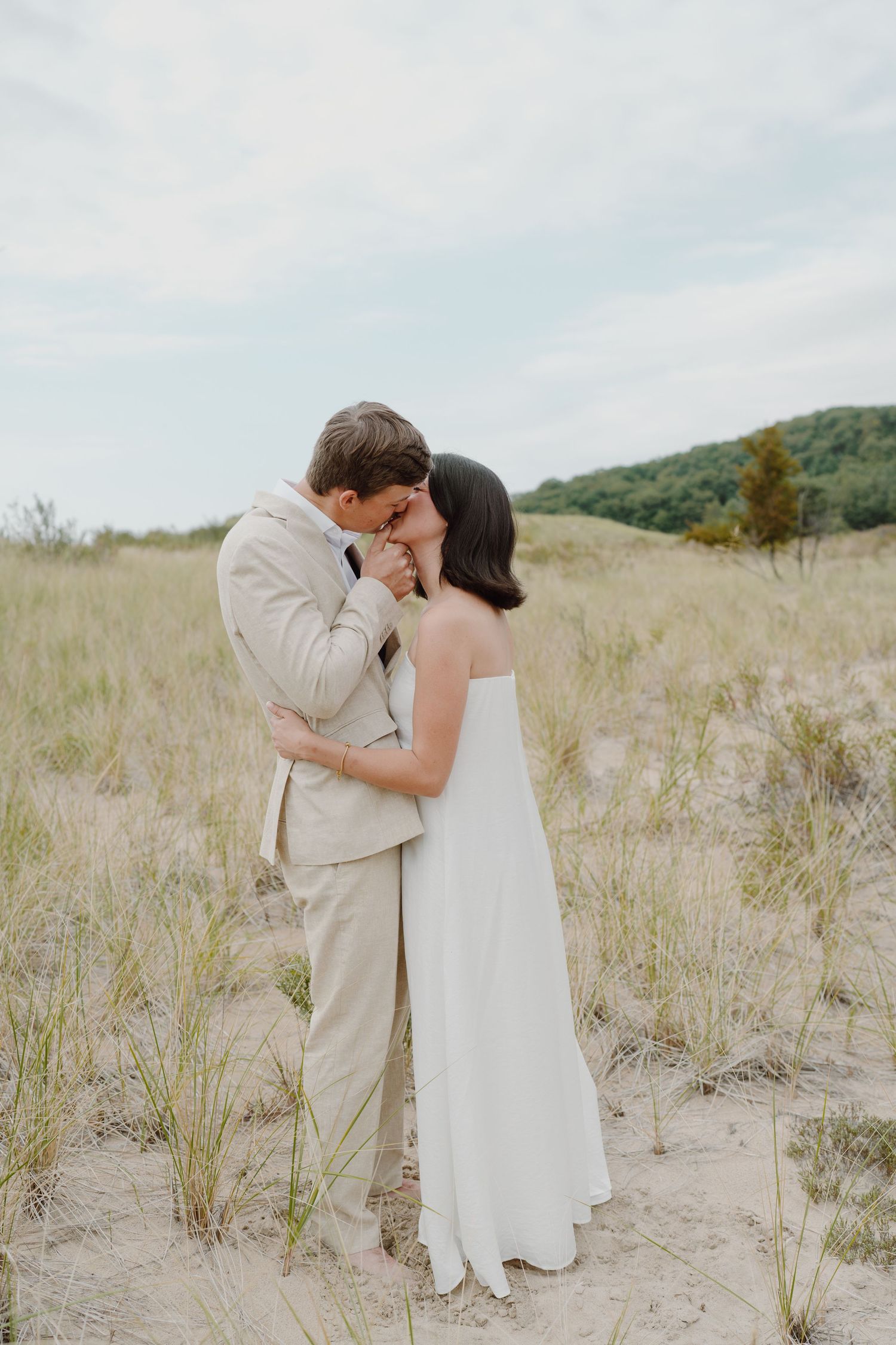 An intimate wedding photo showing a couple embracing on coastal dunes.