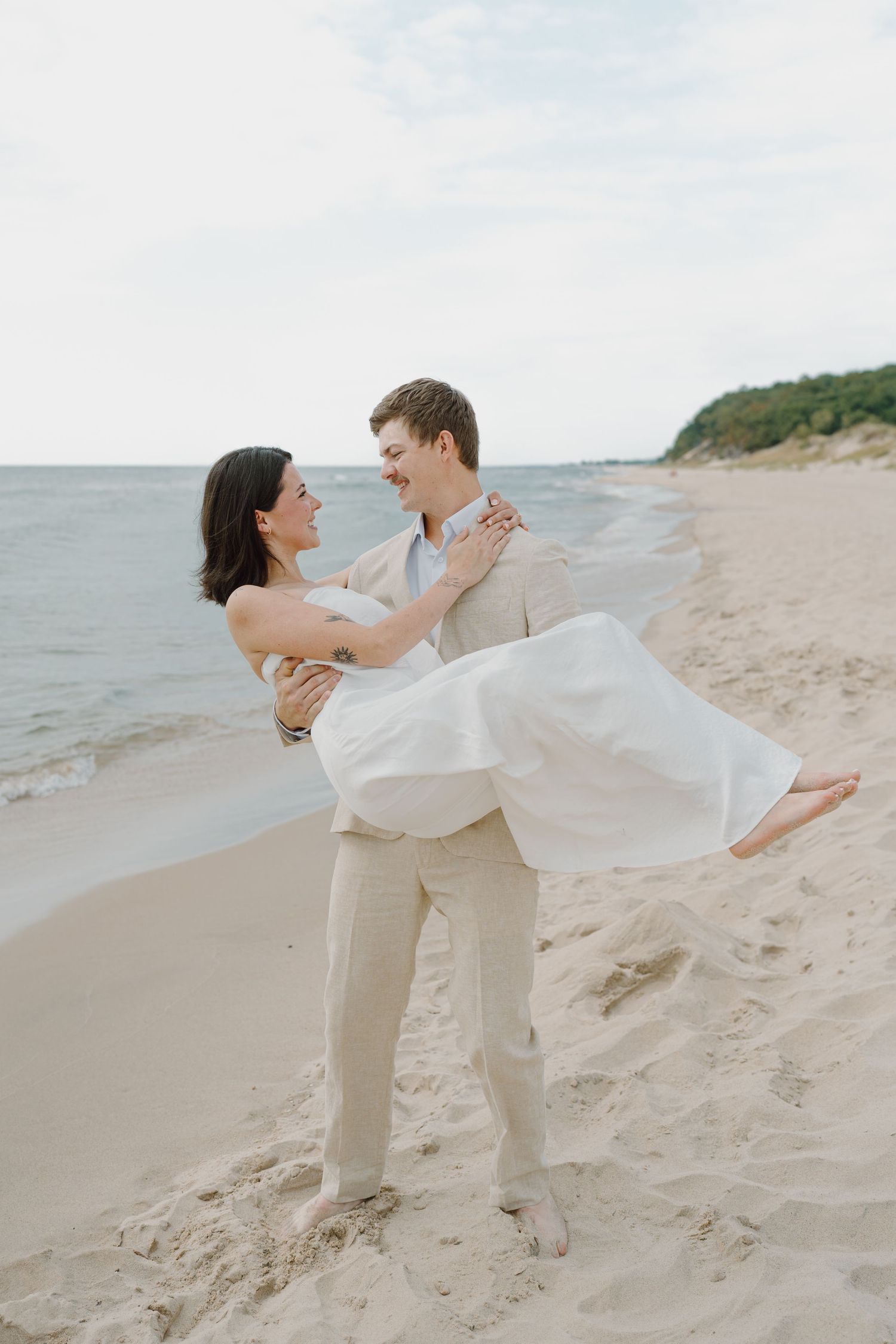 Couple in coordinated outfits dance together on a peaceful beach with gentle waves in background.