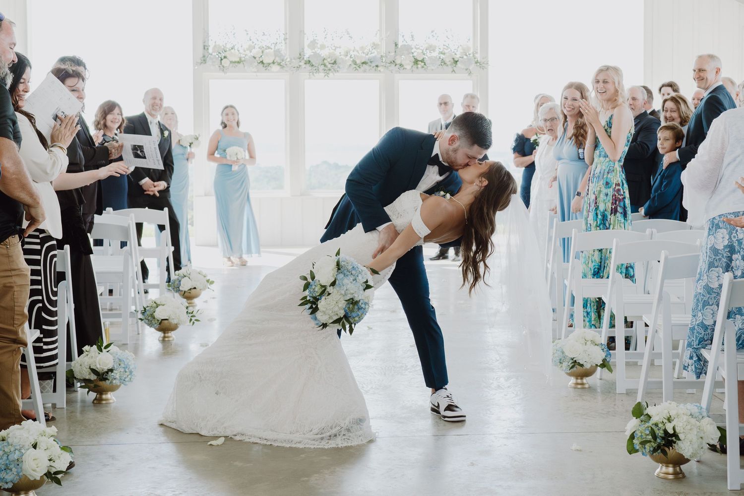 Wedding reception guests celebrate in an elegant white-draped venue with floral arrangements.