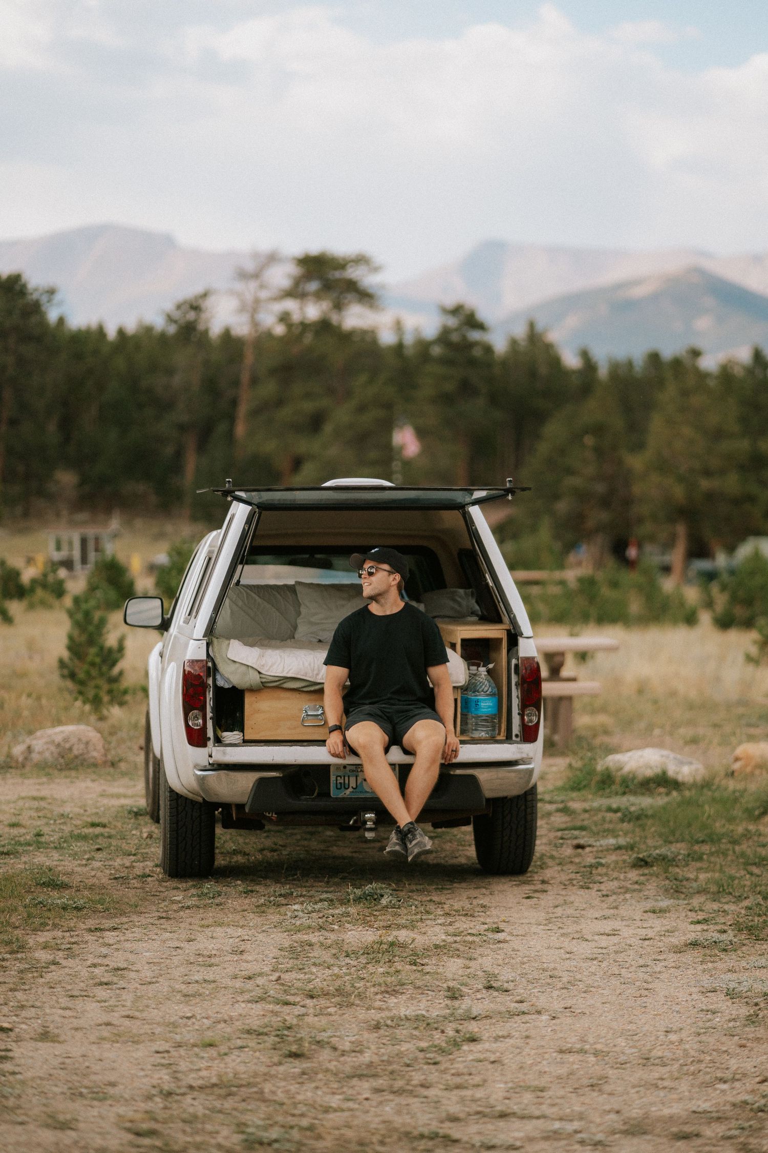 Person relaxing in the back of a pickup truck with mountains in the background.