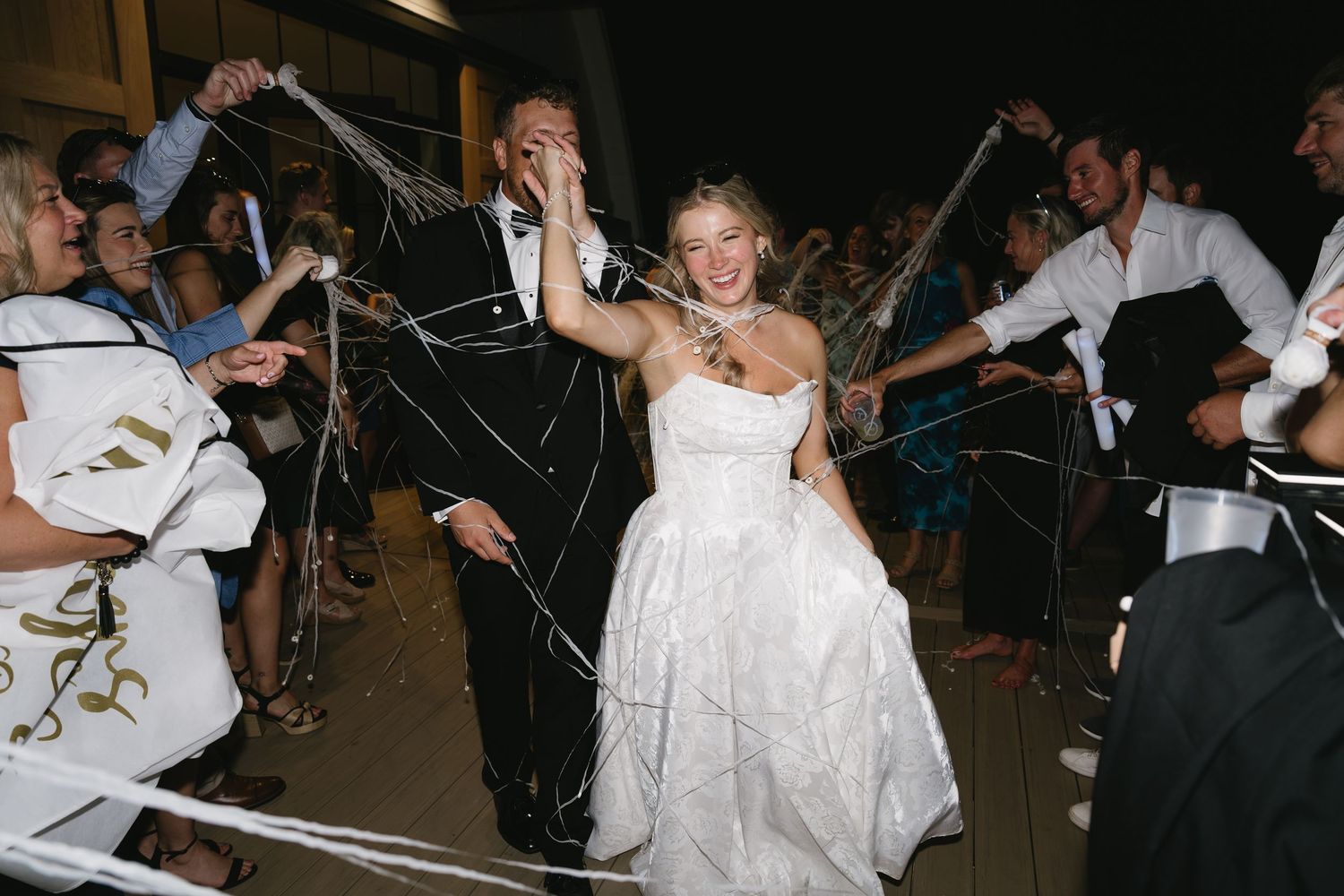 Joyful bride and groom exit wedding reception through cheering guests throwing streamers.