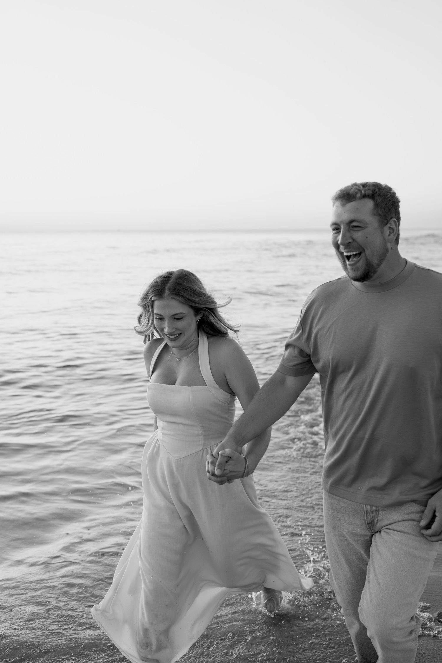 Black and white photo of joyful couple laughing while walking on beach.