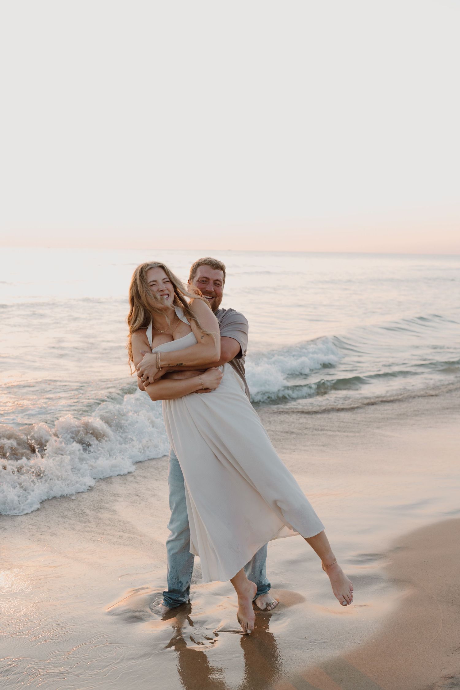 A romantic couple plays in the surf at sunset, splashing in the shallow waves.