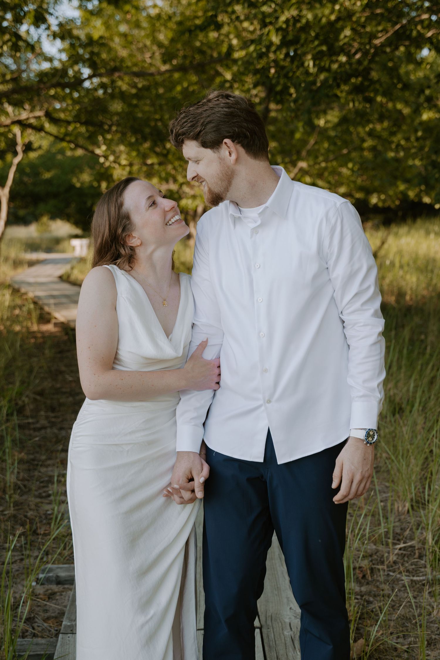 Couple in formal white and navy attire sharing tender moments in a natural setting.