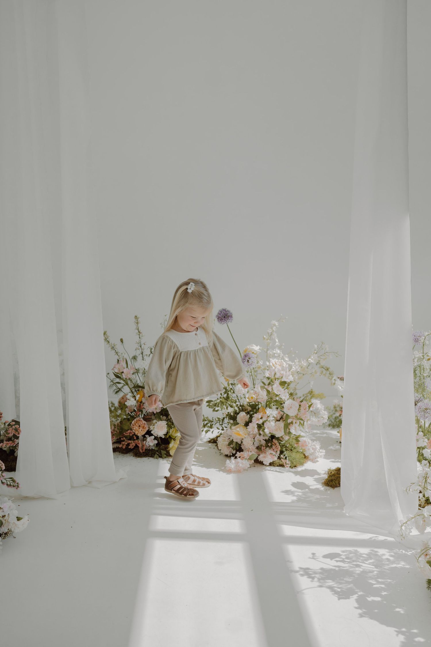 Bright minimalist studio space with delicate floral arrangements and flowing white fabric creating shadows.