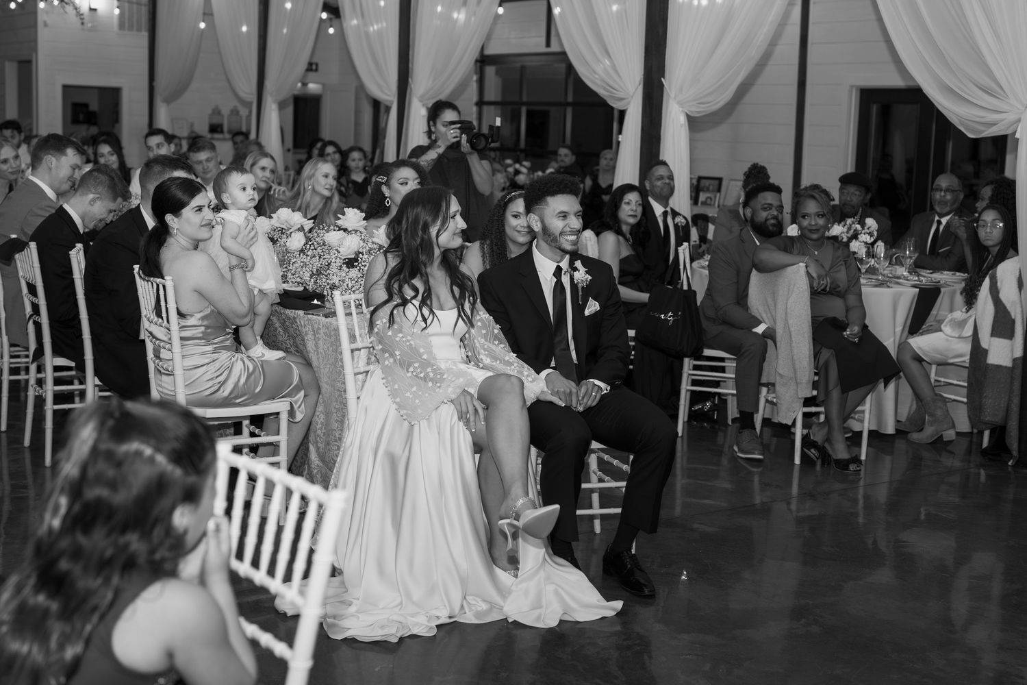 Wedding reception guests watch the couple's dance from white chairs in an elegantly decorated venue.