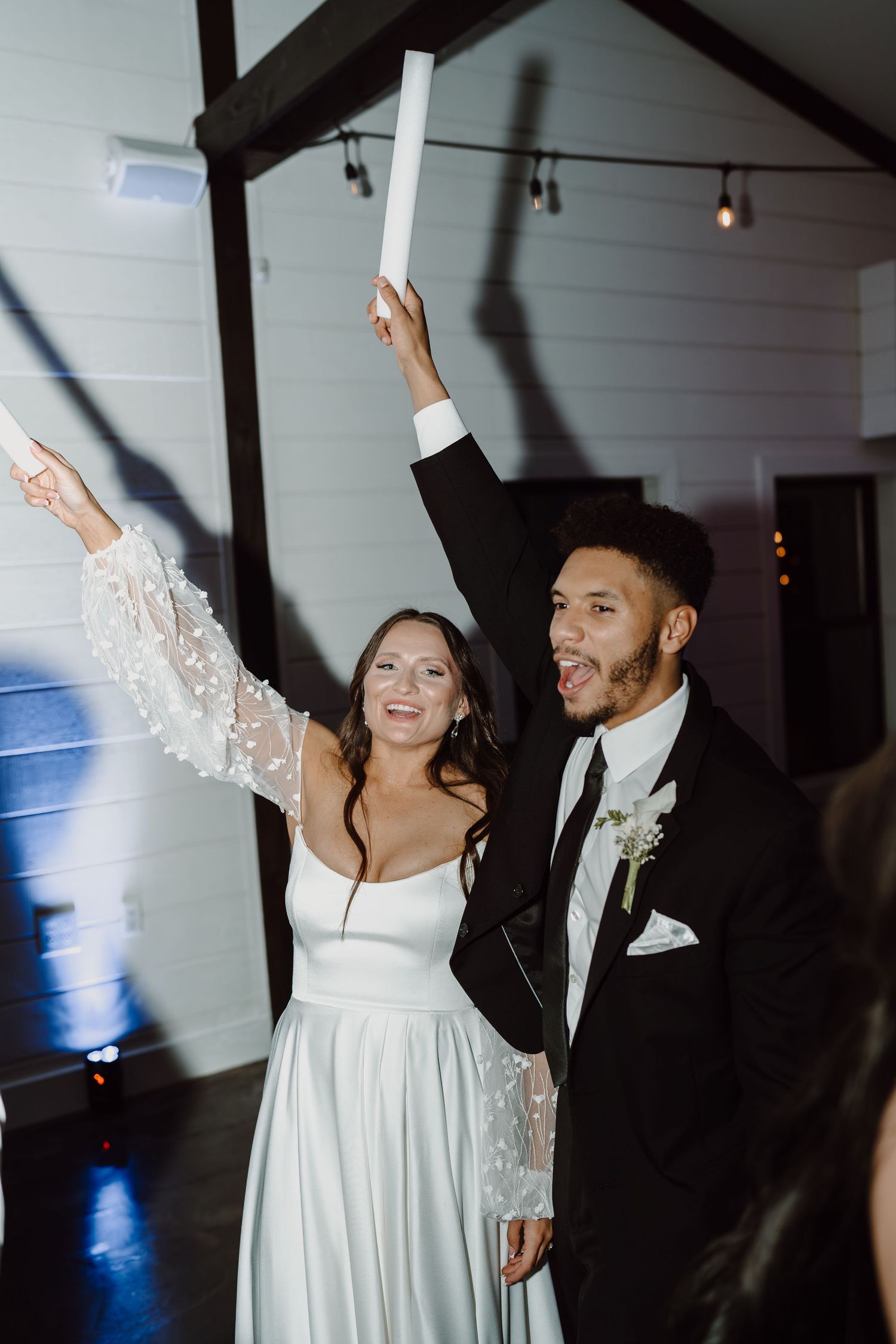 Wedding couple celebrates joyfully with LED foam sticks during their reception.
