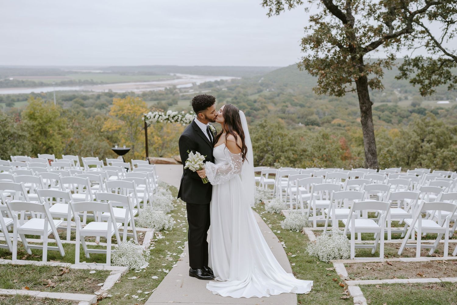 An elegant hilltop wedding ceremony site with rows of white chairs and panoramic views.