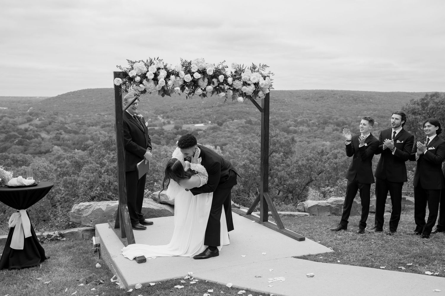 Black and white photo of a wedding ceremony on a scenic overlook with mountains in the background.