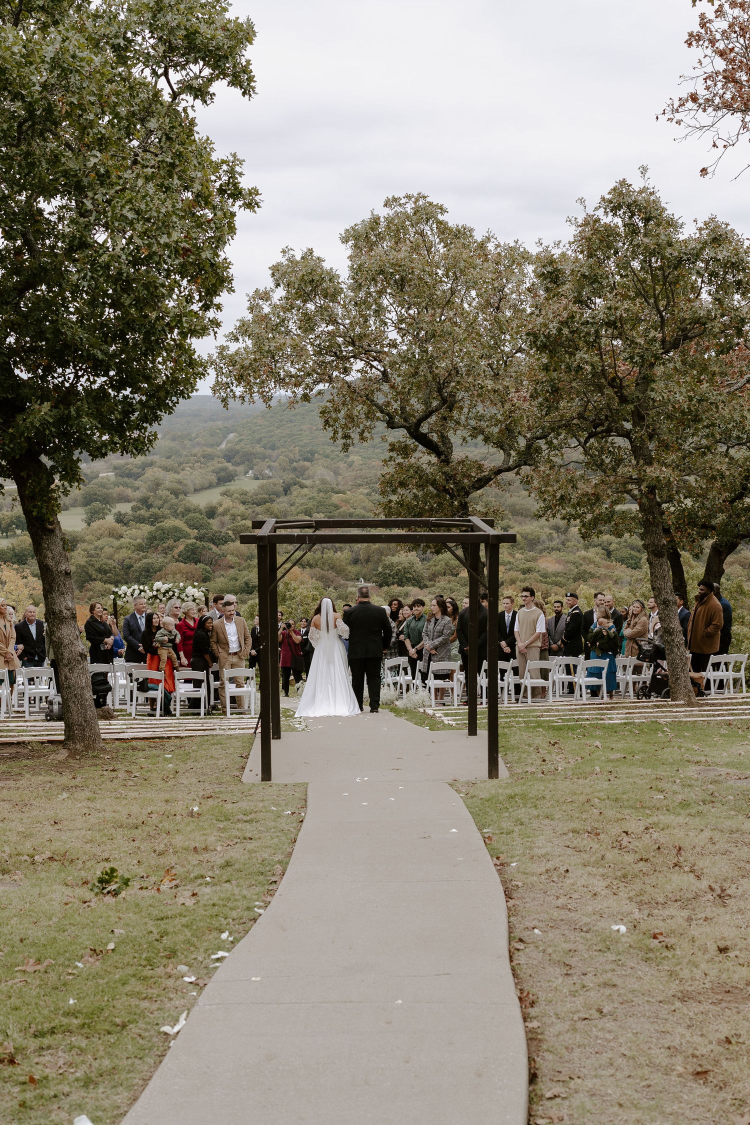 White chairs arranged on a grassy hillside for an outdoor wedding ceremony with trees in the background.