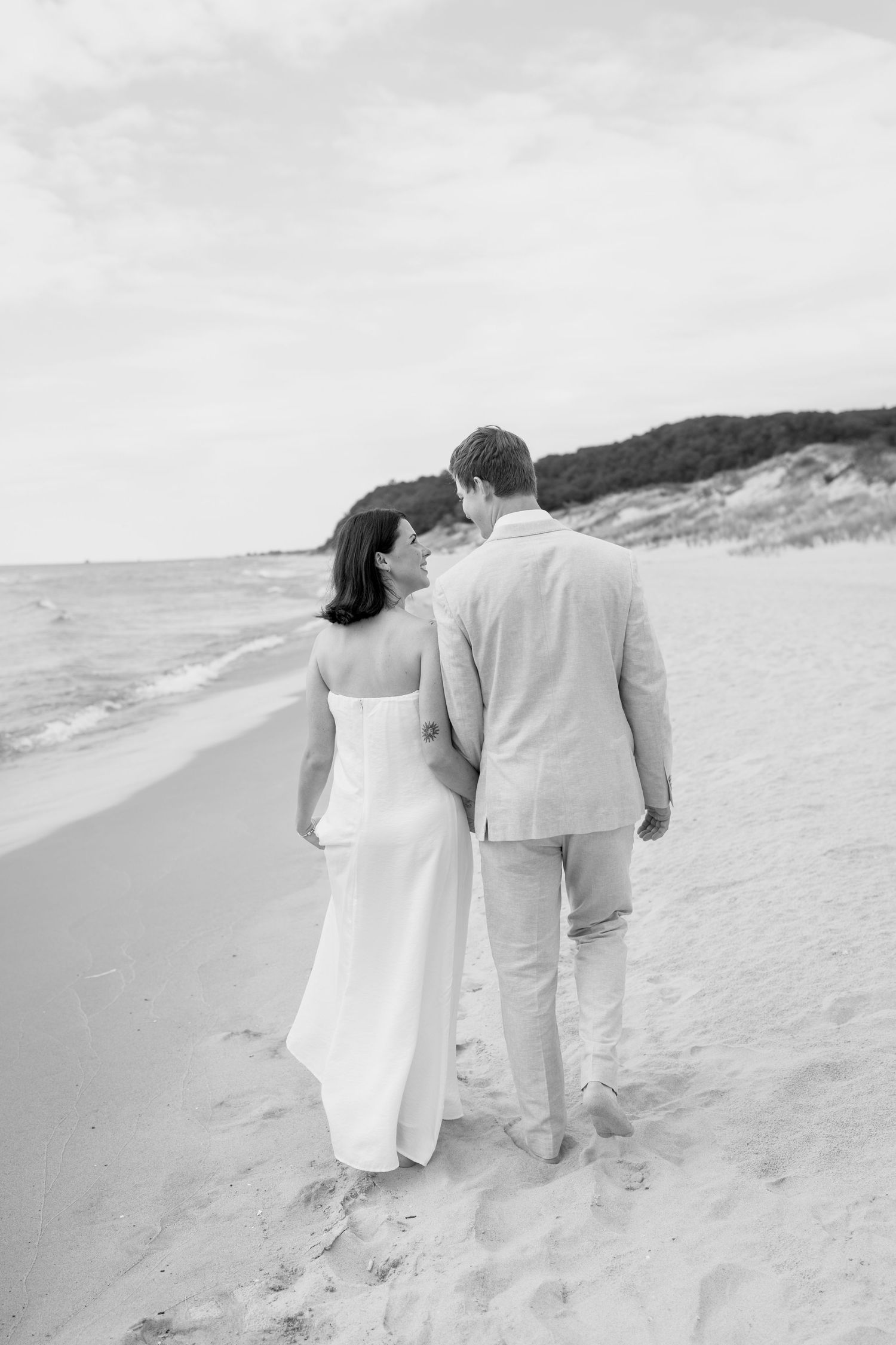 A couple walking hand in hand on a sandy beach in black and white photography.