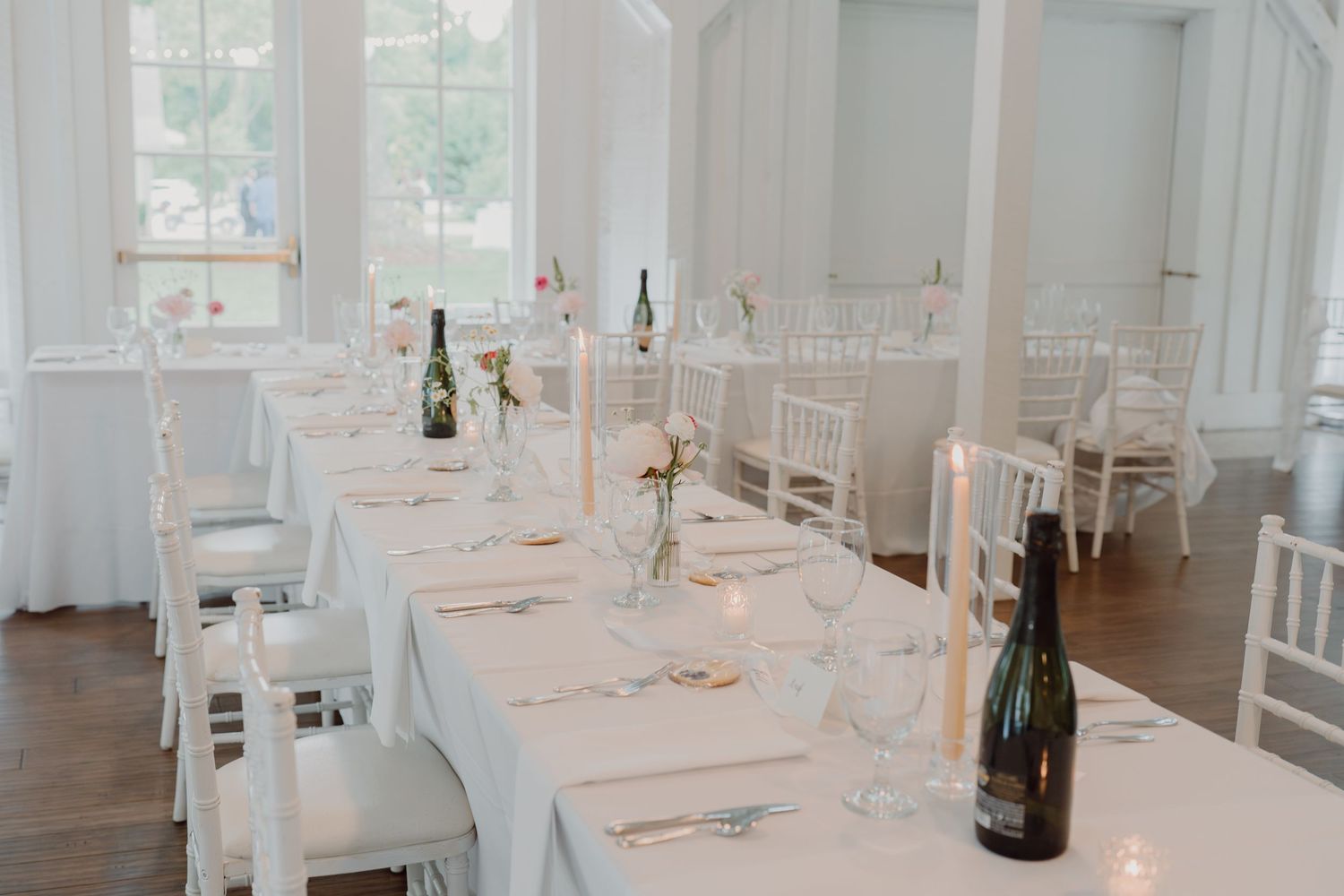Bright white reception hall with long tables set for formal dining.