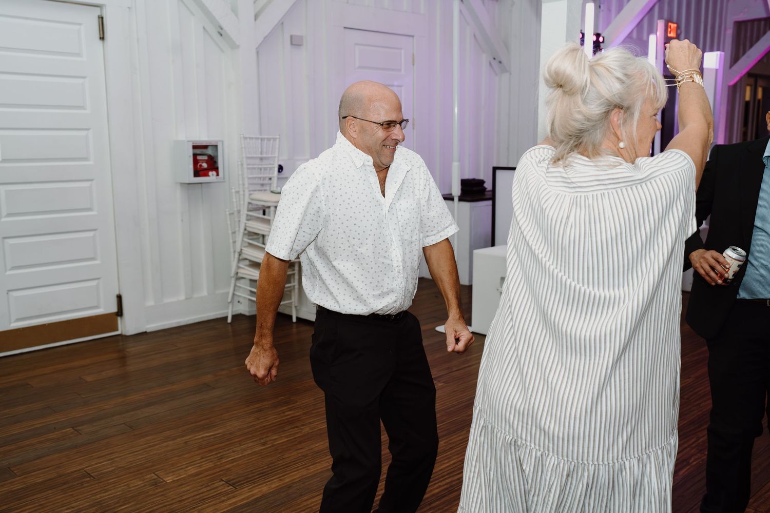 Guests dancing together at a wedding reception in a rustic white-beamed venue.