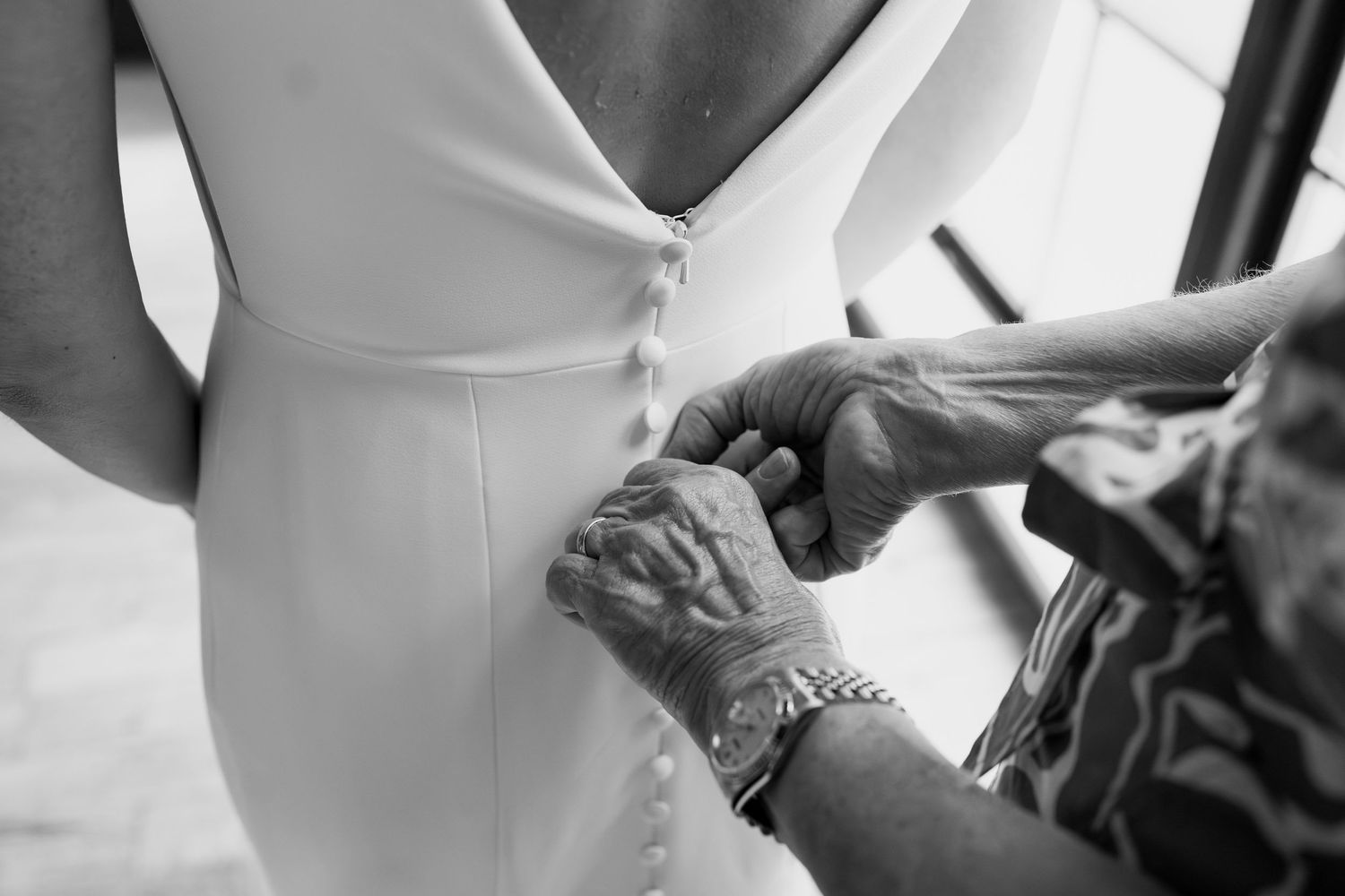 Detailed black and white shot of hands fastening buttons on a wedding gown.