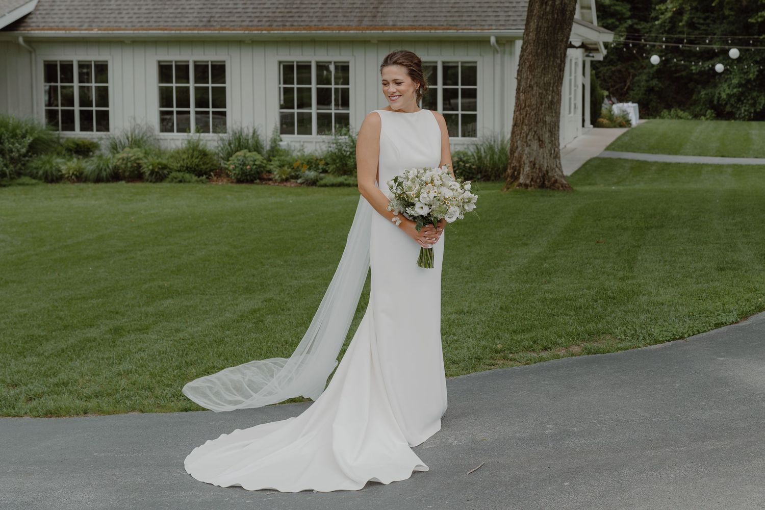 A serene wedding scene with a white dress trailing on a curved driveway near a traditional building.