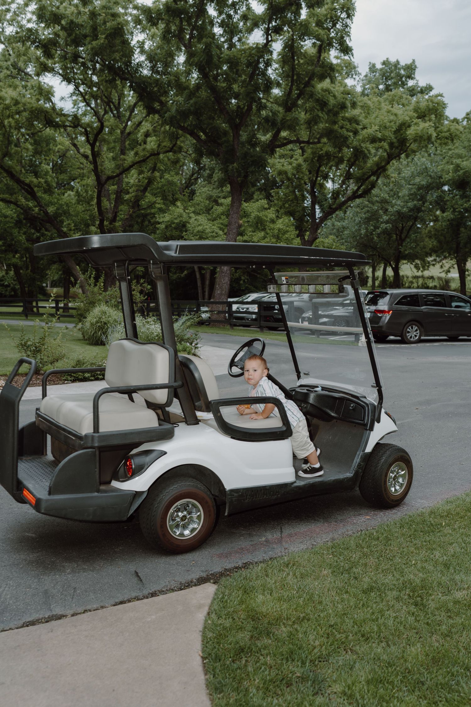 Vintage white golf cart parked on a curved driveway surrounded by green trees.
