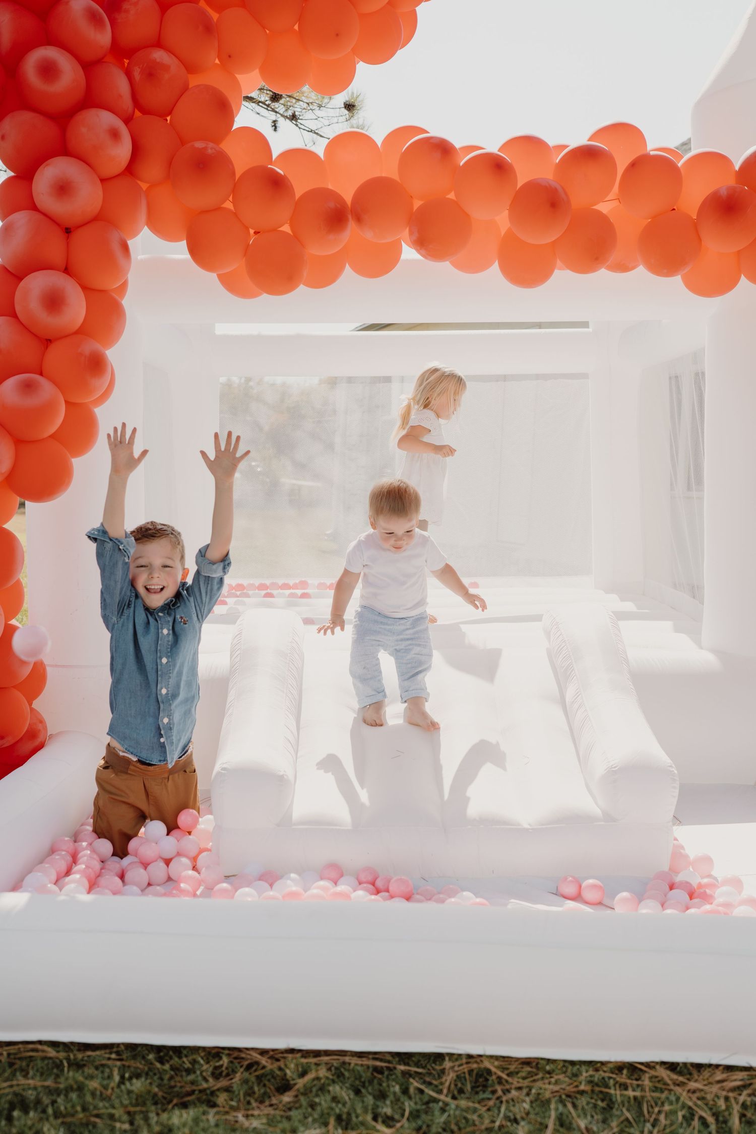 Kids jumping and playing in a white bounce house decorated with red balloons.