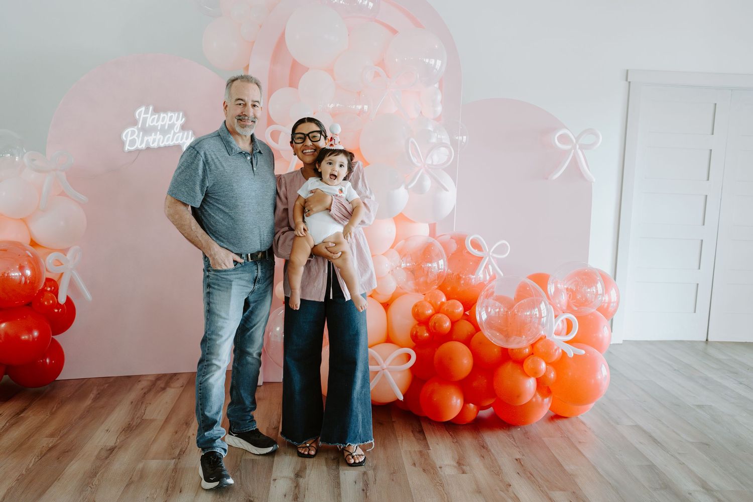 Family portrait session with festive balloon backdrop in coral and pink tones.