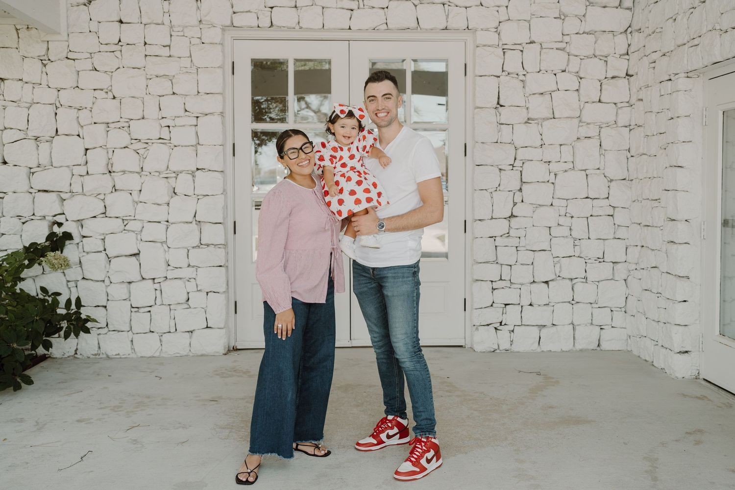 Family playfully posing against white stone wall in casual attire.
