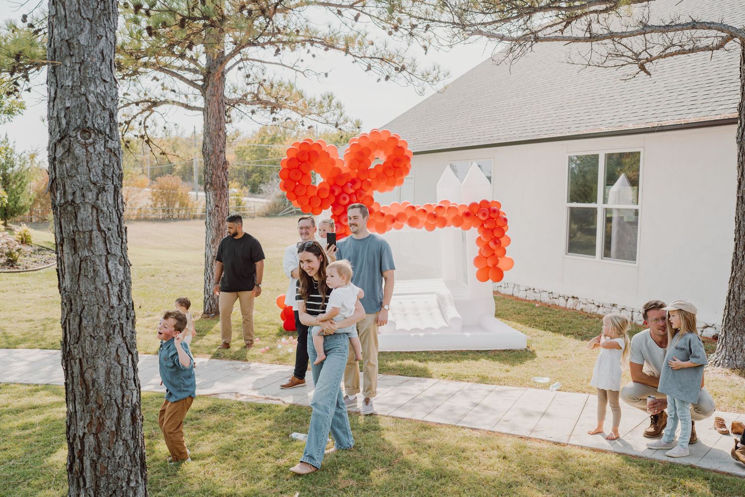 People stand near a pine tree with a red heart balloon display visible in the background.