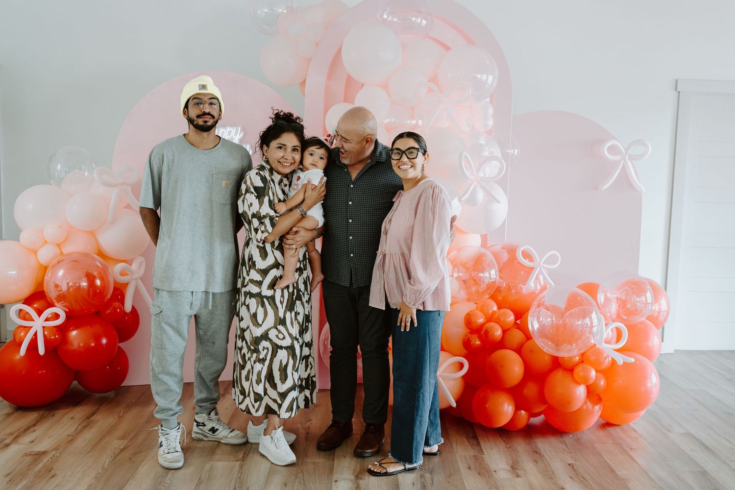 Family portrait in front of an elegant balloon arch with pink and coral gradient.