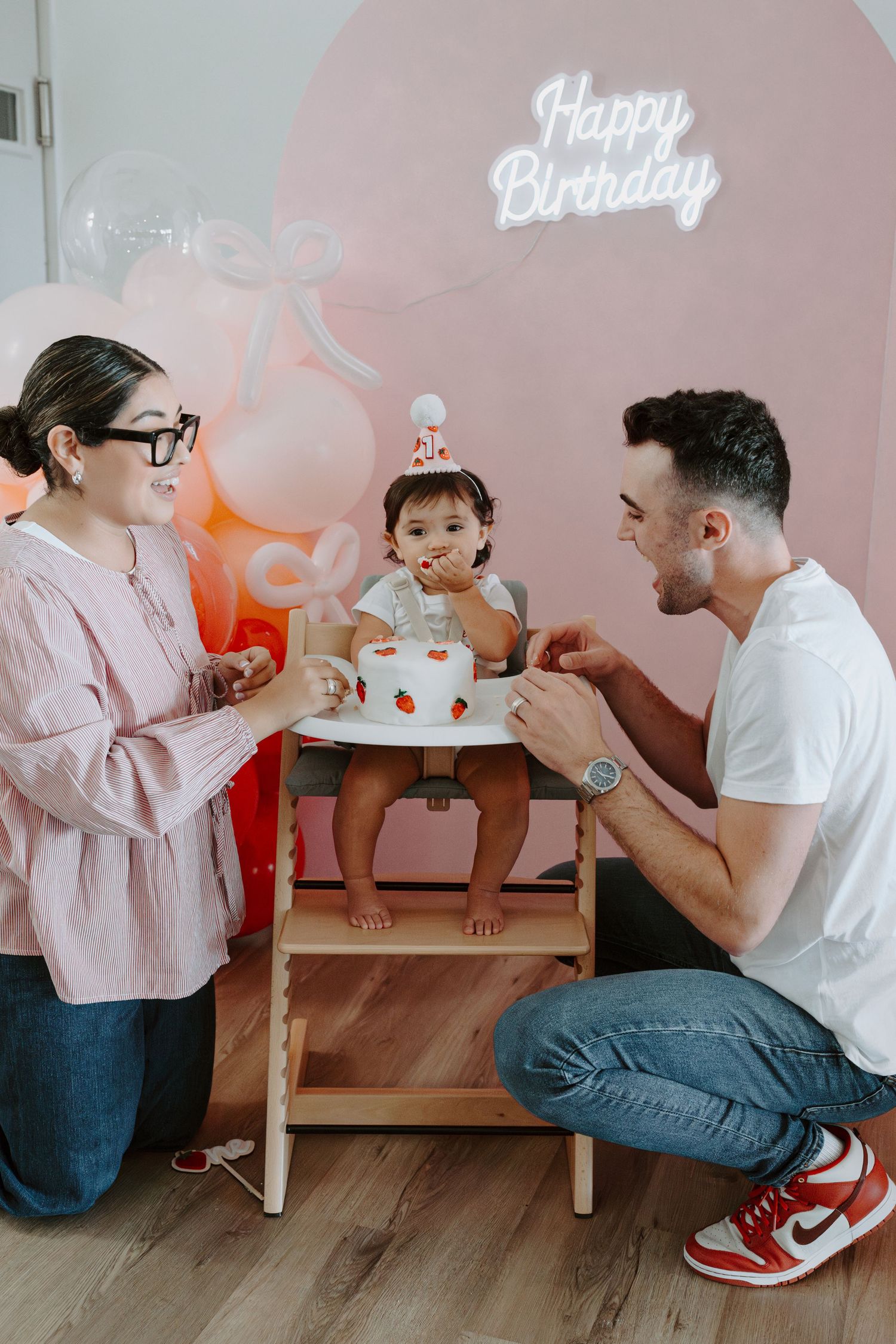 Birthday party scene with pink decor and balloons featuring a small high chair.