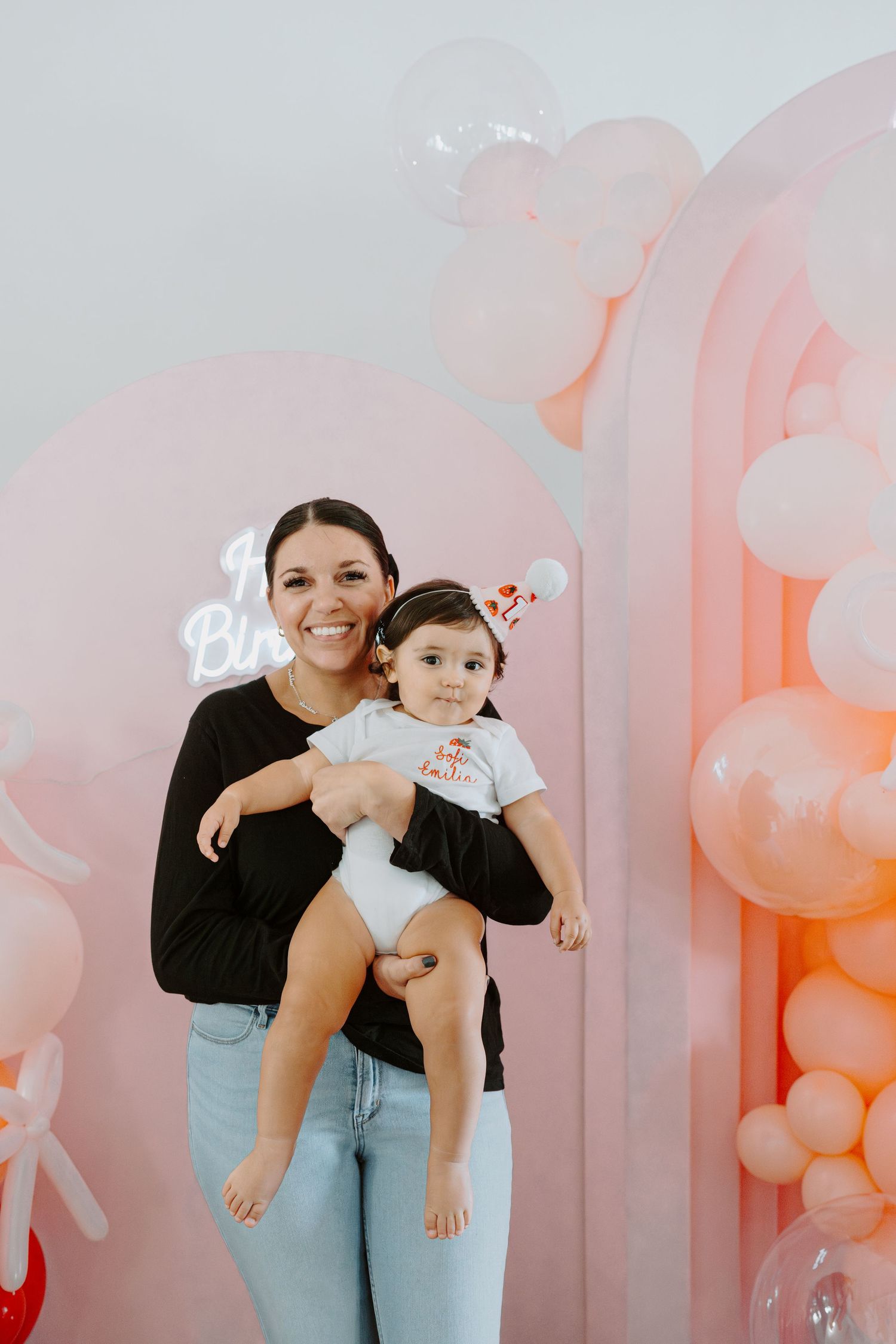 Studio portraits against a pink balloon wall backdrop in casual attire.