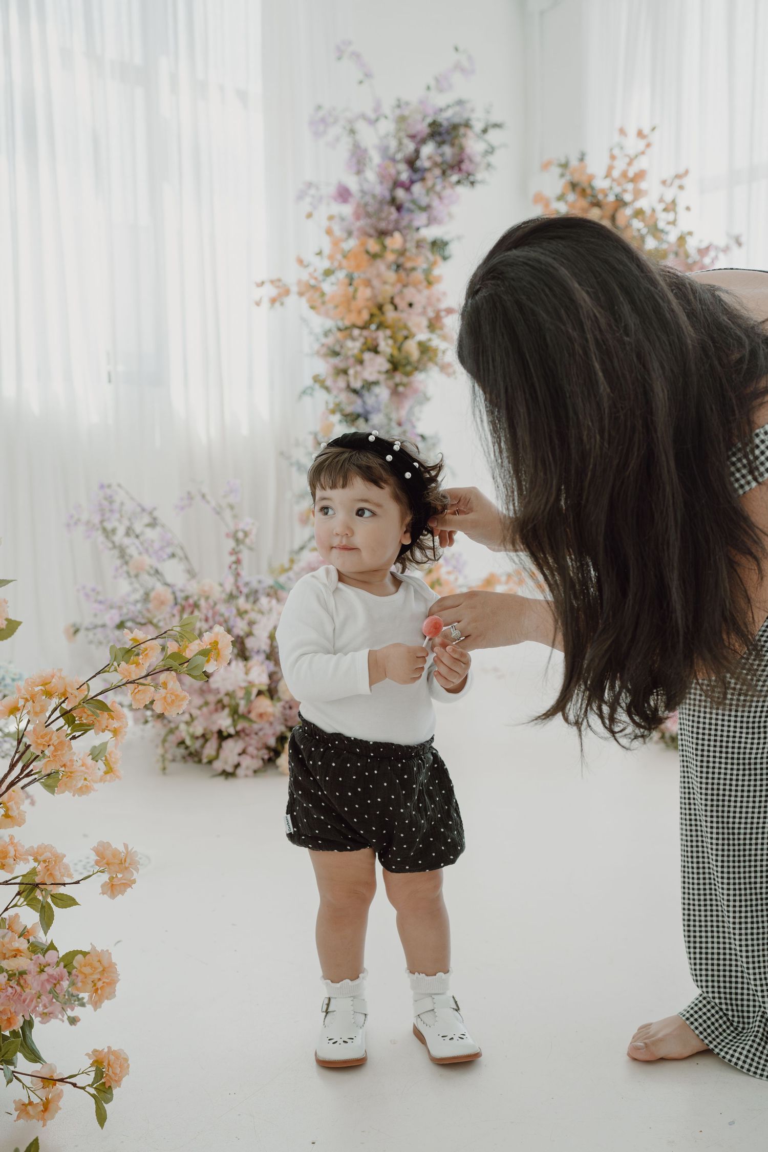 Sweet interaction between toddler and adult in white studio with floral decorations.