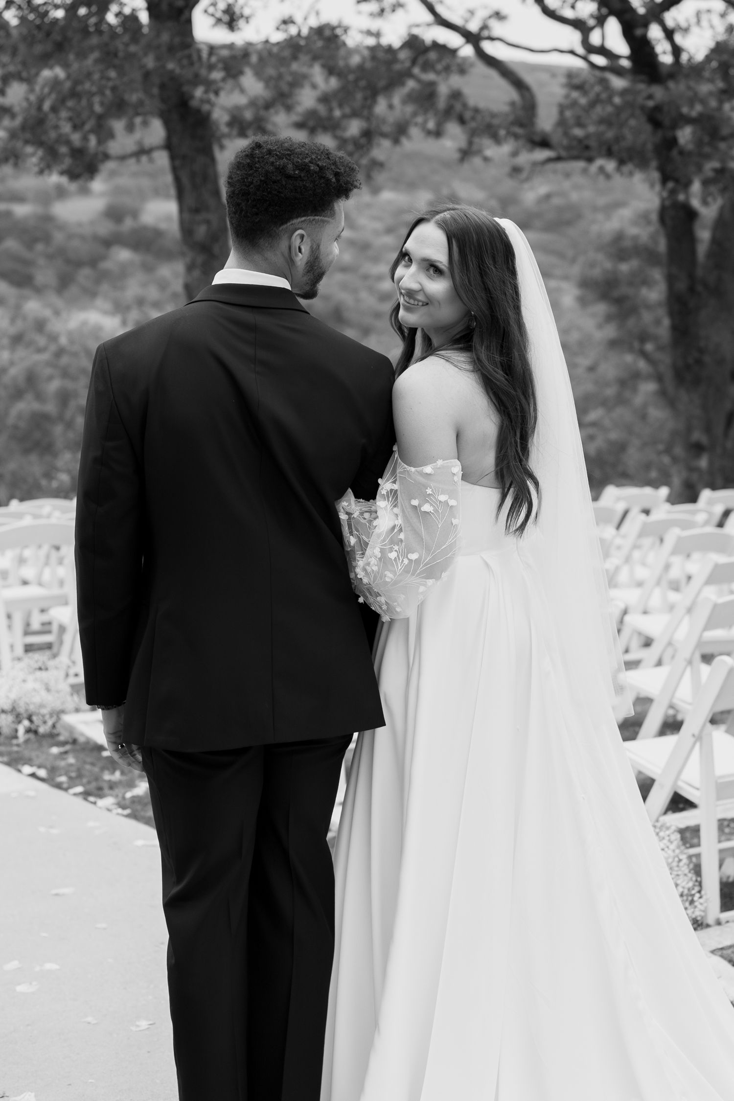 A black and white photo of a couple walking through their outdoor wedding ceremony space.