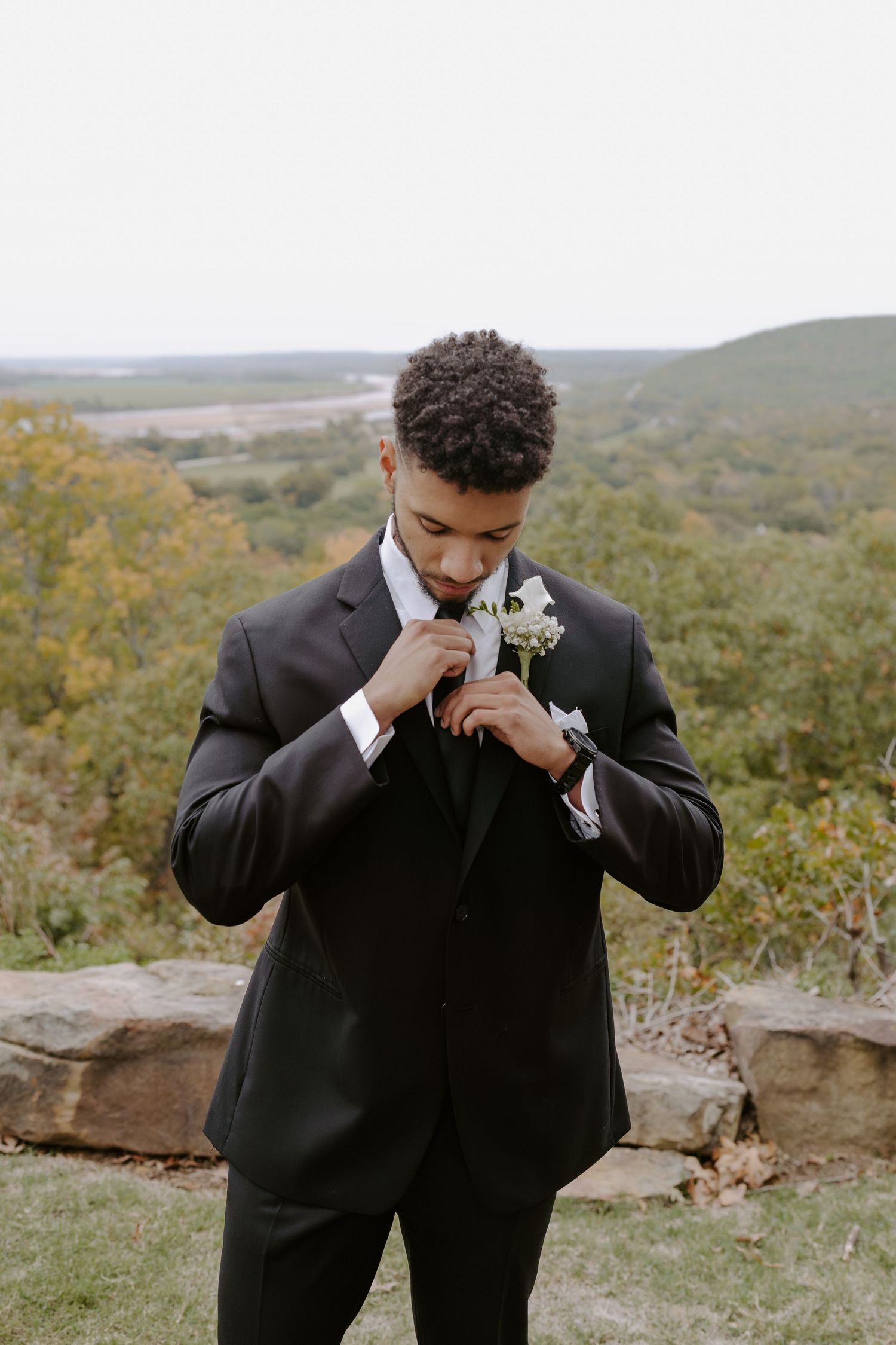 Wedding party member in black suit shows emotion during outdoor photography session.