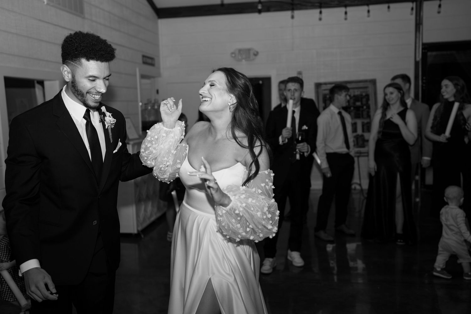 Wedding party dancing and celebrating in a modern white-walled venue.