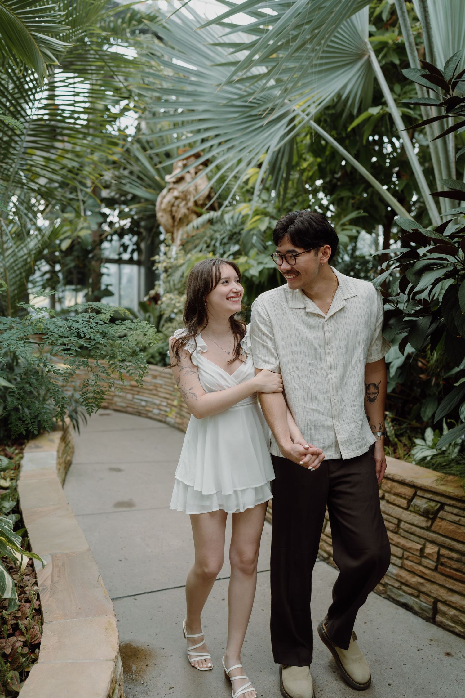 A couple strolls together along a path in a lush indoor garden setting.