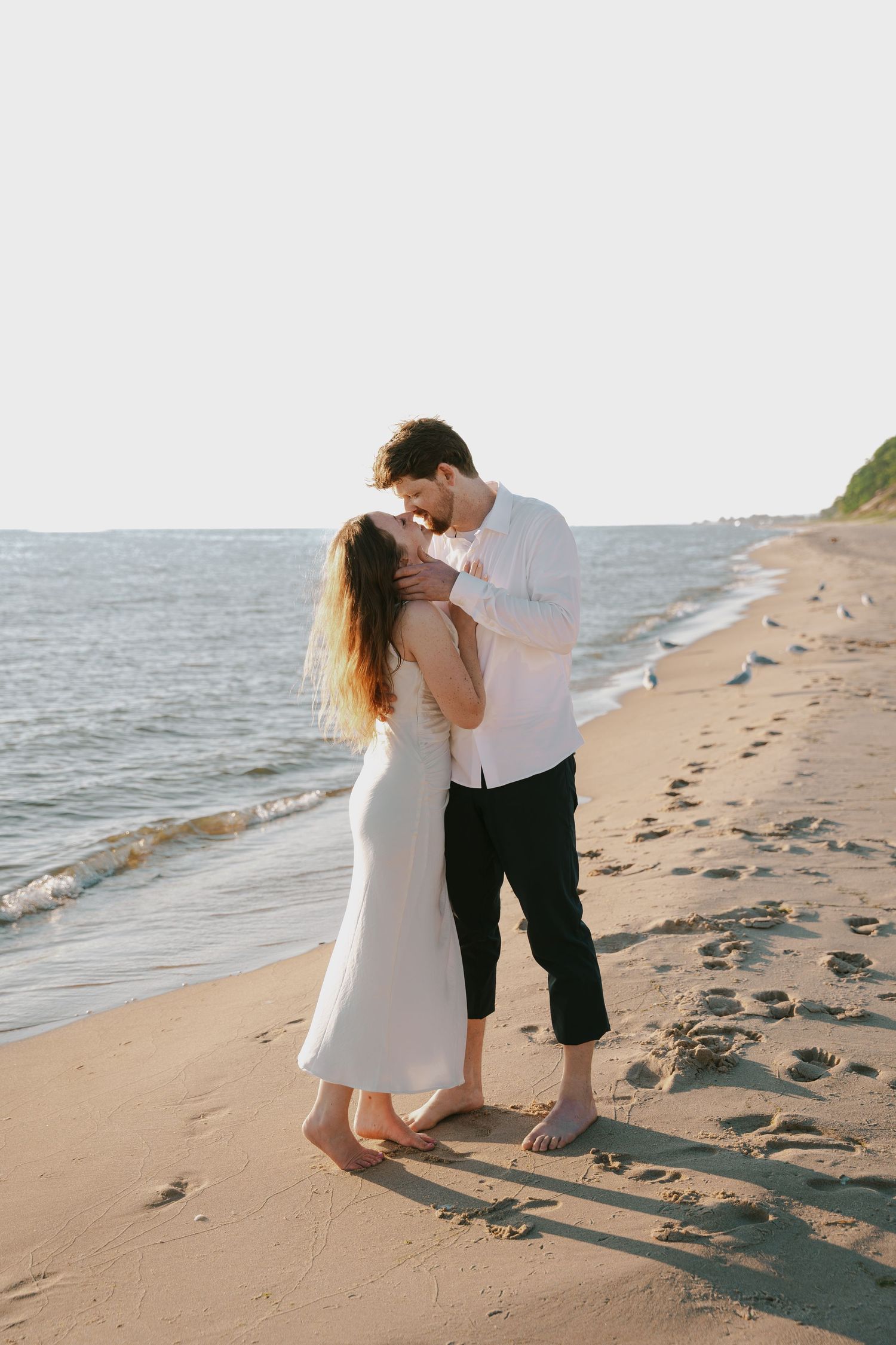 Romantic couple embraces on a sandy beach at sunset with ocean waves in the background.