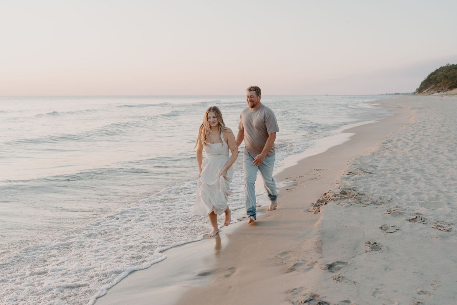 A couple strolls barefoot on a sandy beach during golden hour with gentle waves rolling in.