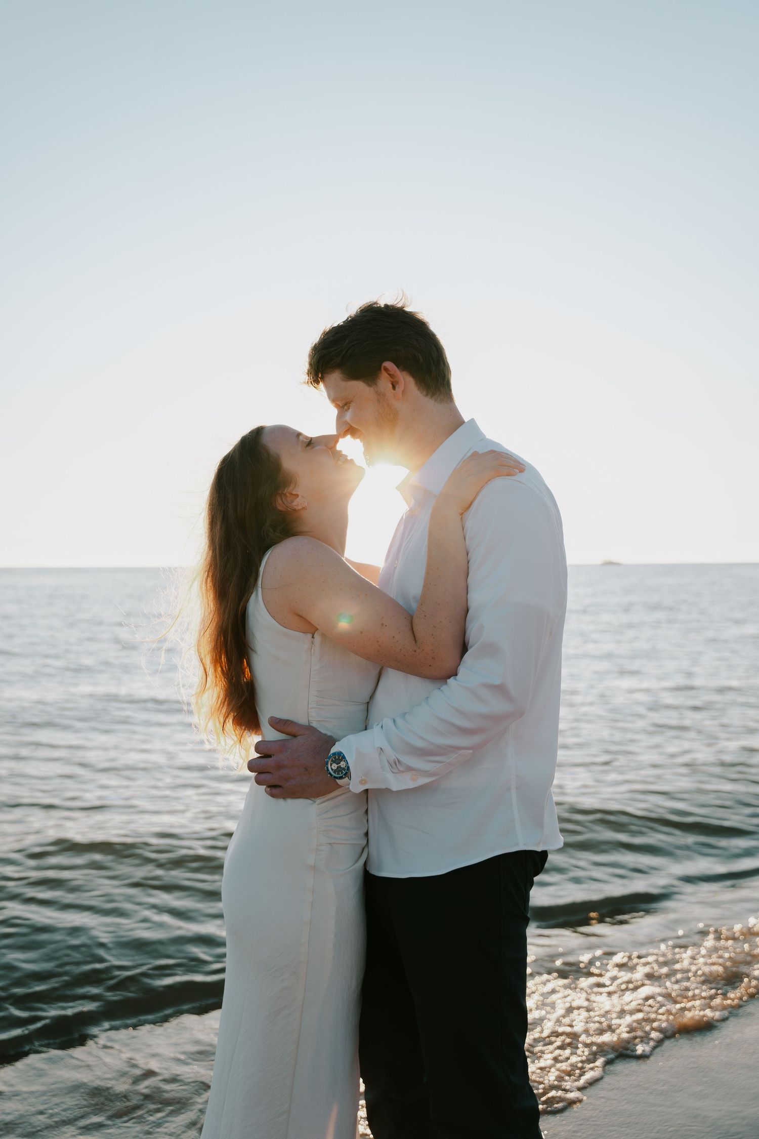Sunset silhouette of couple sharing intimate moment on beach with waves behind them.