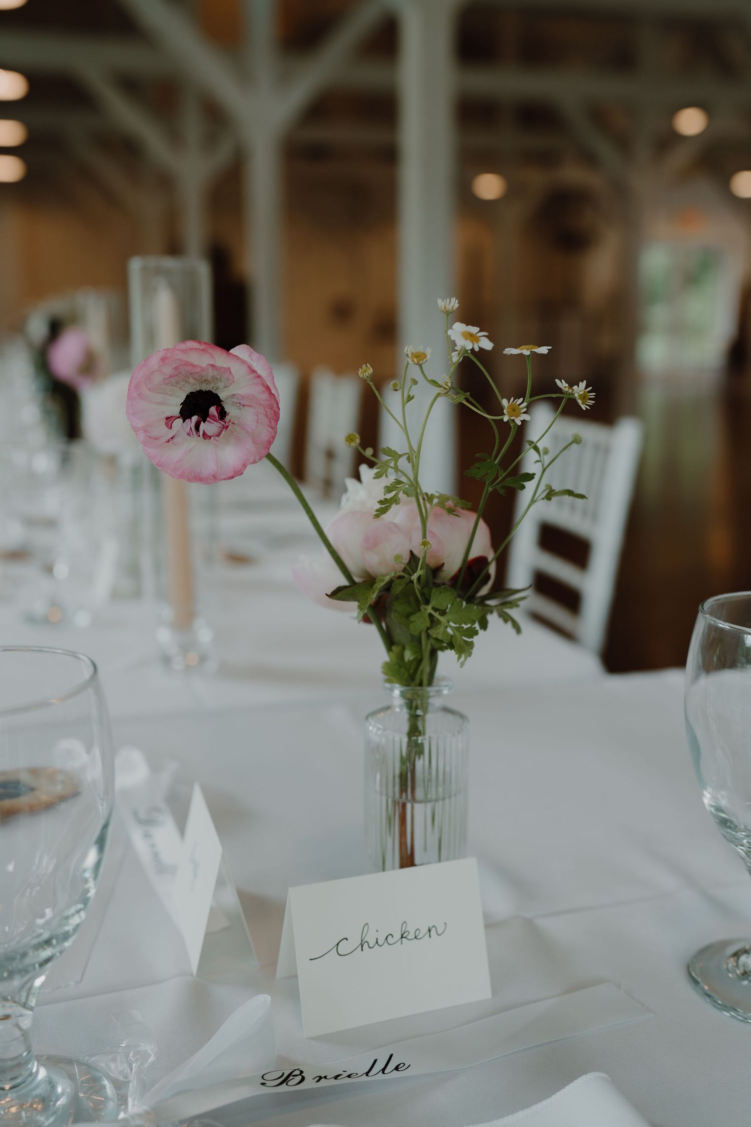 Delicate pink flowers in small vases accent white table settings at an elegant event.