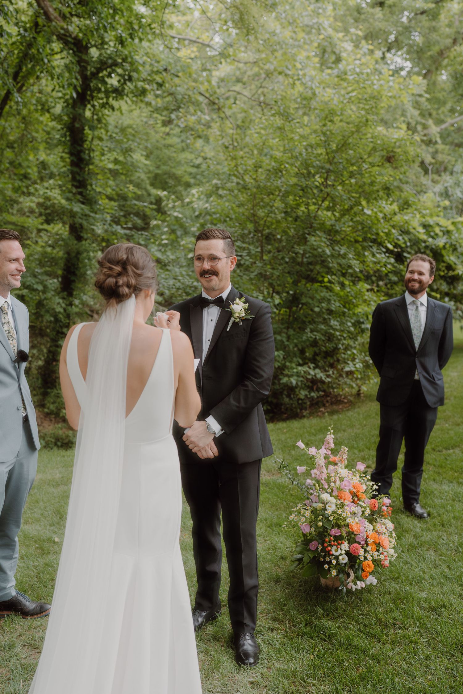 Intimate outdoor wedding ceremony with guests watching in a green woodland setting.