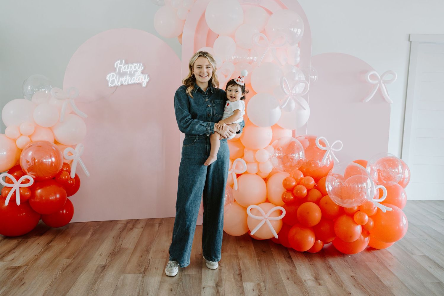 Birthday party setup with an elegant coral and pink balloon arch against a white wall.