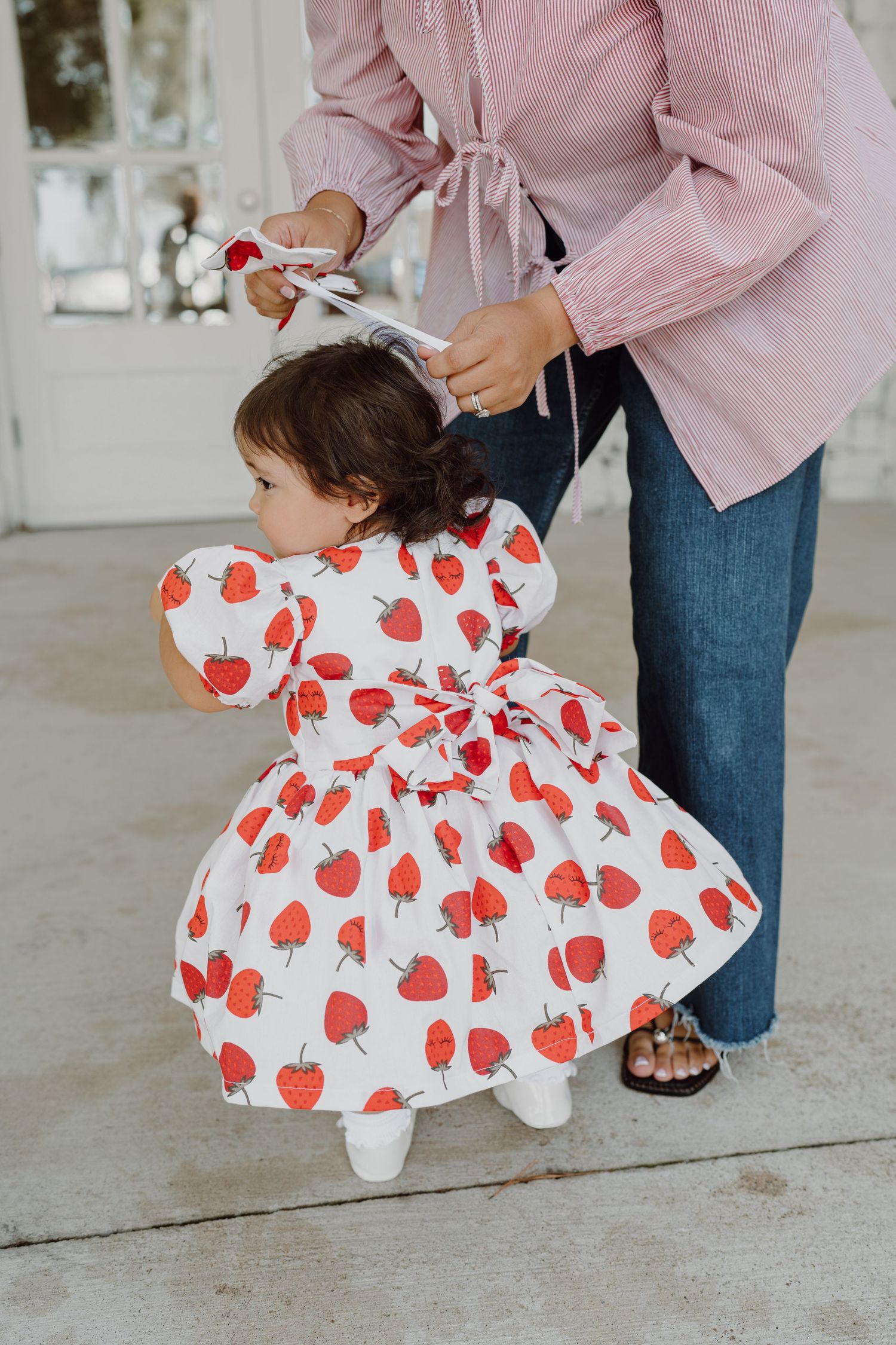 Parent adjusting child's heart-print dress against stone wall background.