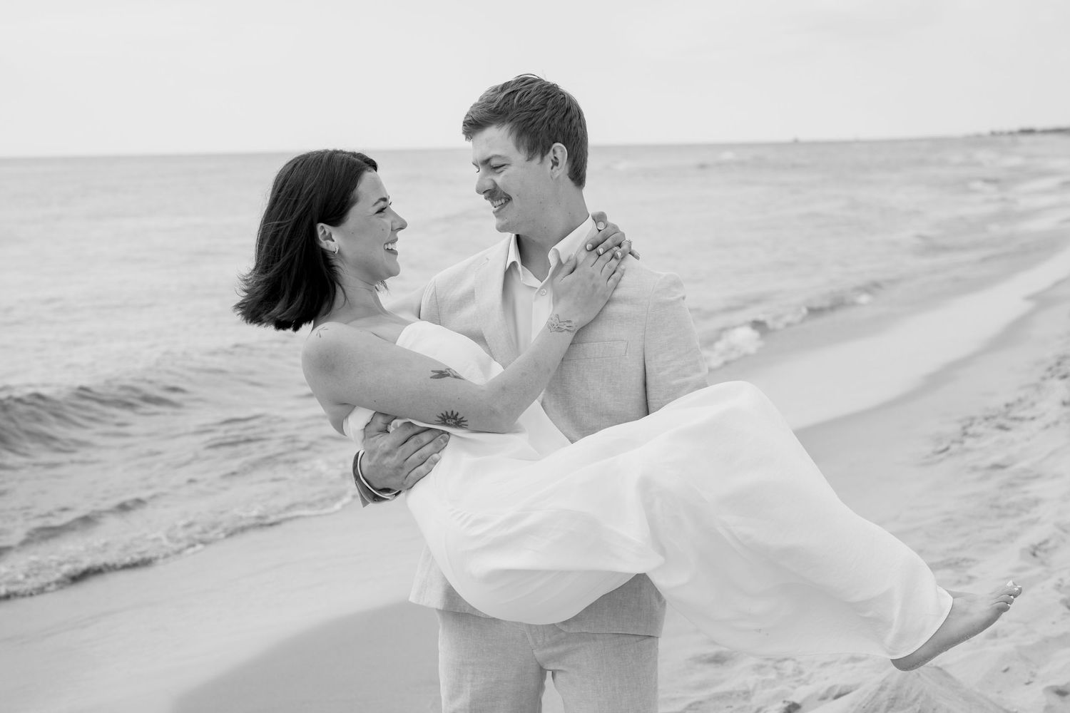 Romantic couple in white and beige embrace on a sandy beach during a dreamy photoshoot.