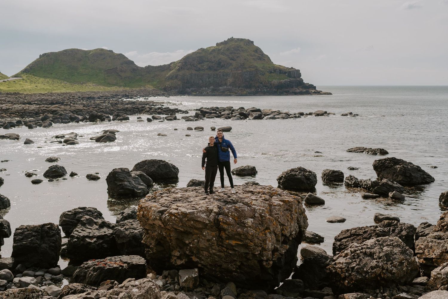 Rocky coastal landscape with black boulders scattered along a misty shoreline.