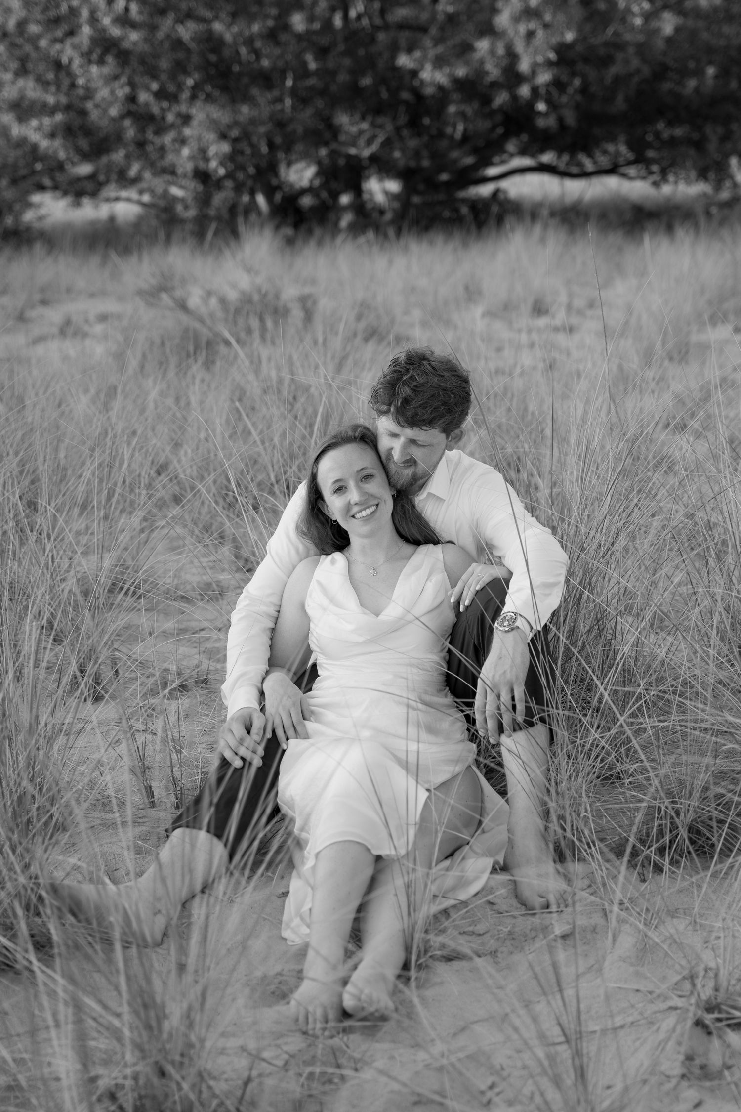 A black and white portrait of a couple relaxing in a grassy meadow.