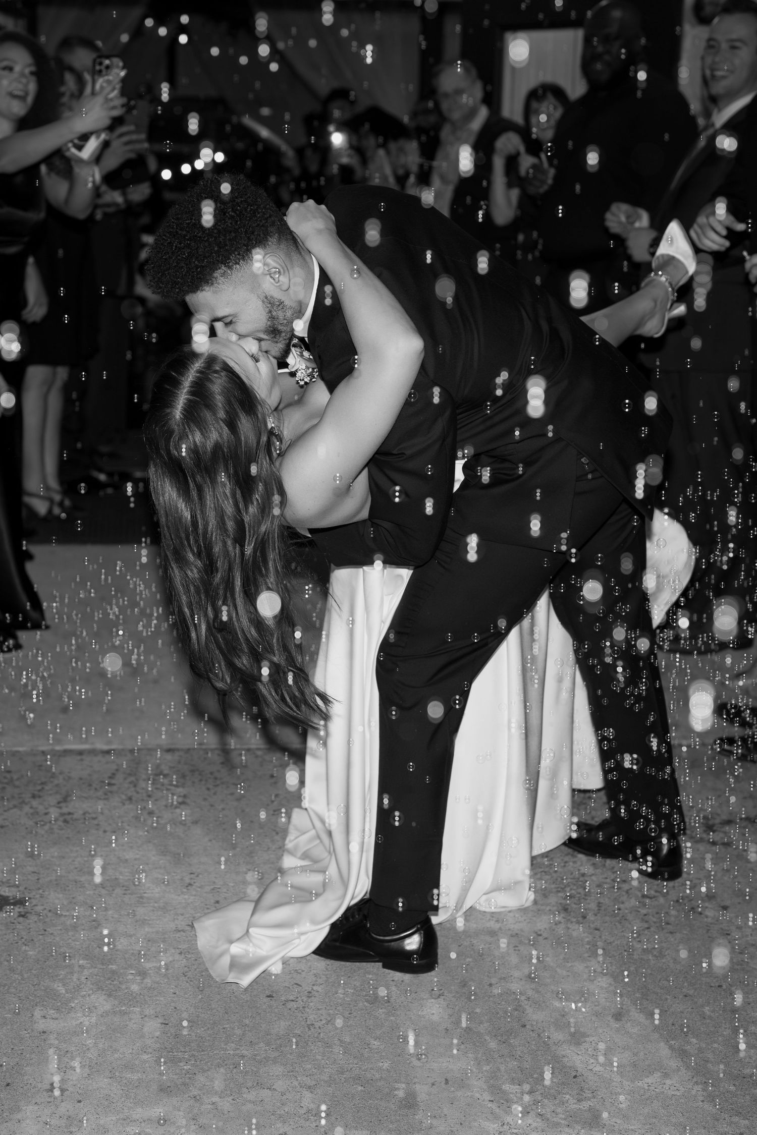 Black and white photo of wedding guests dancing with confetti falling on the dance floor.
