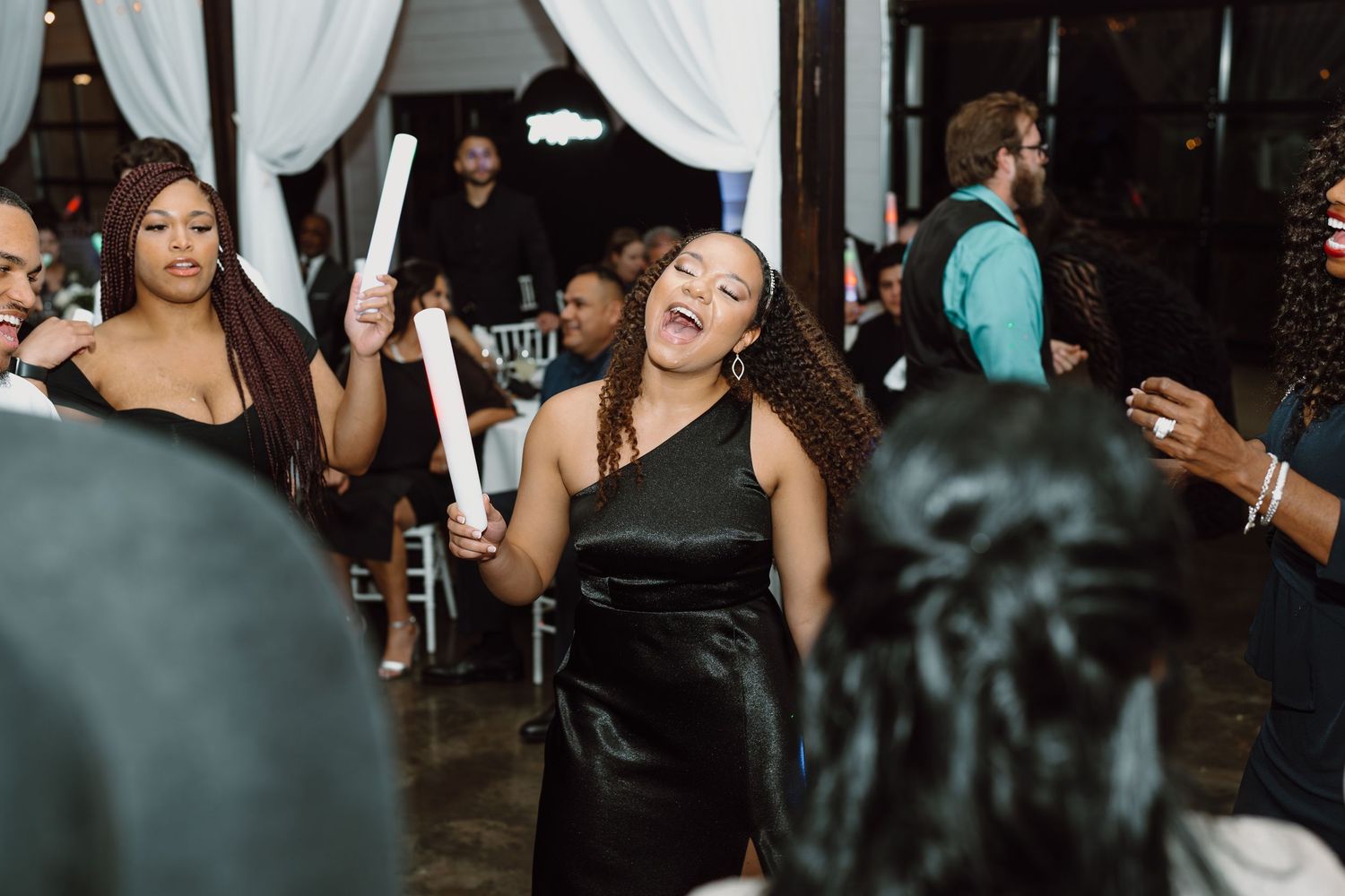 Wedding guests dancing and celebrating at indoor reception with white drape decorations.