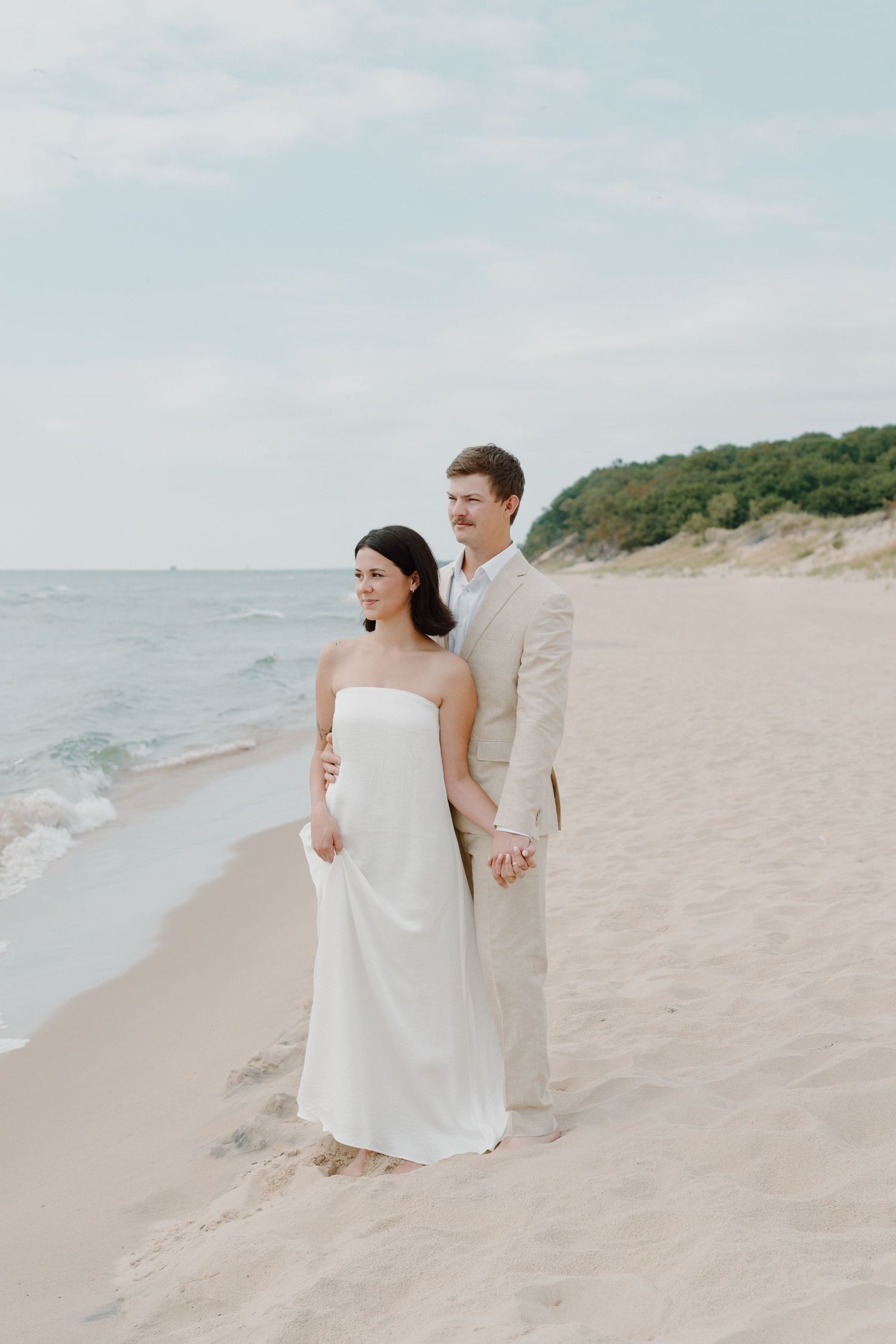 A couple shares a joyful moment together on a sandy beach with waves and green cliffs in the background.