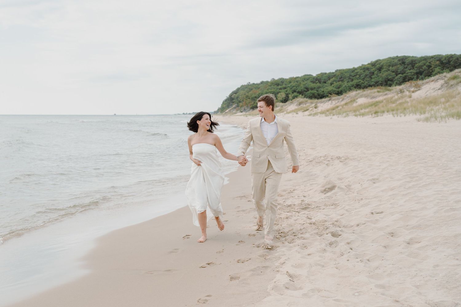 Two people in light colored attire dance and play together on a peaceful beach setting.
